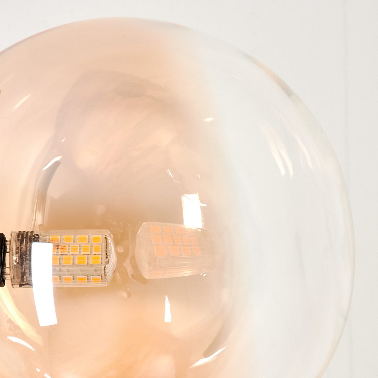 Nahaufnahme einer bernsteinfarbenen Glaskugel mit LED-Licht, vor weißem Hintergrund.