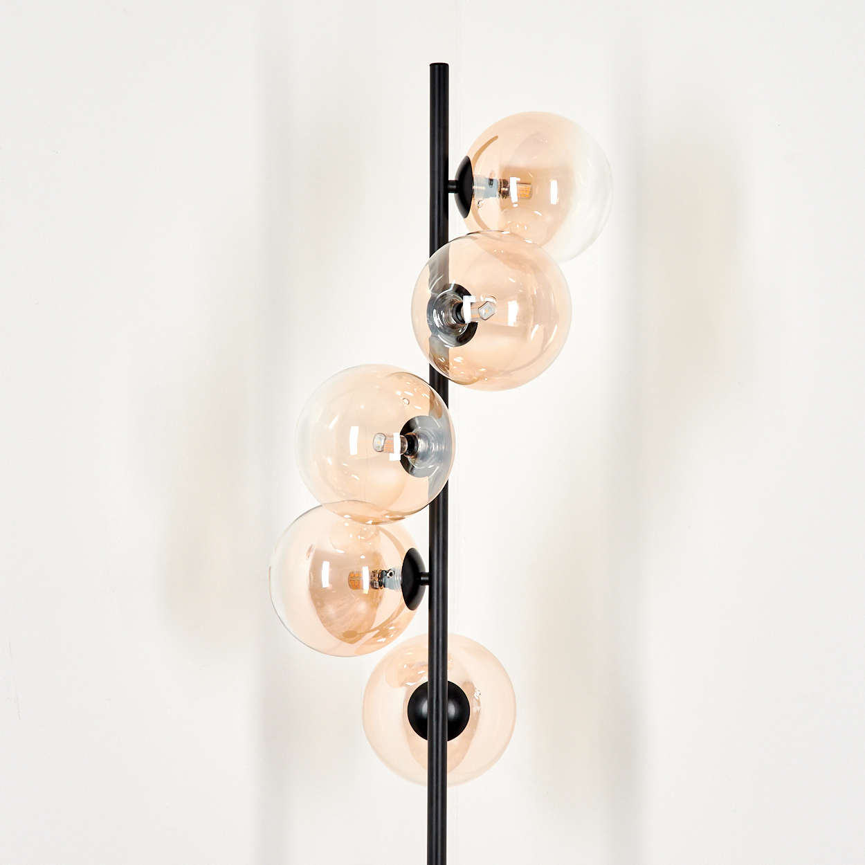 Nahaufnahme einer schwarzen Stehlampe mit fünf orangefarbenen Glaskugelschirmen vor einer weißen Wand.