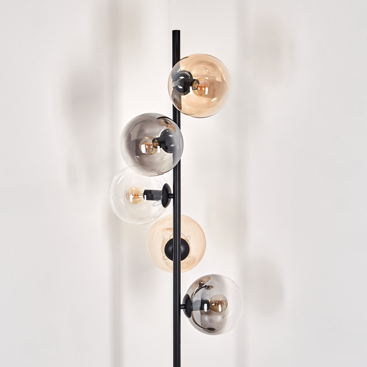 Nahaufnahme einer schwarzen Stehlampe mit fünf Glaskugelschirmen. Die Lampe steht vor einem weißen Hintergrund.