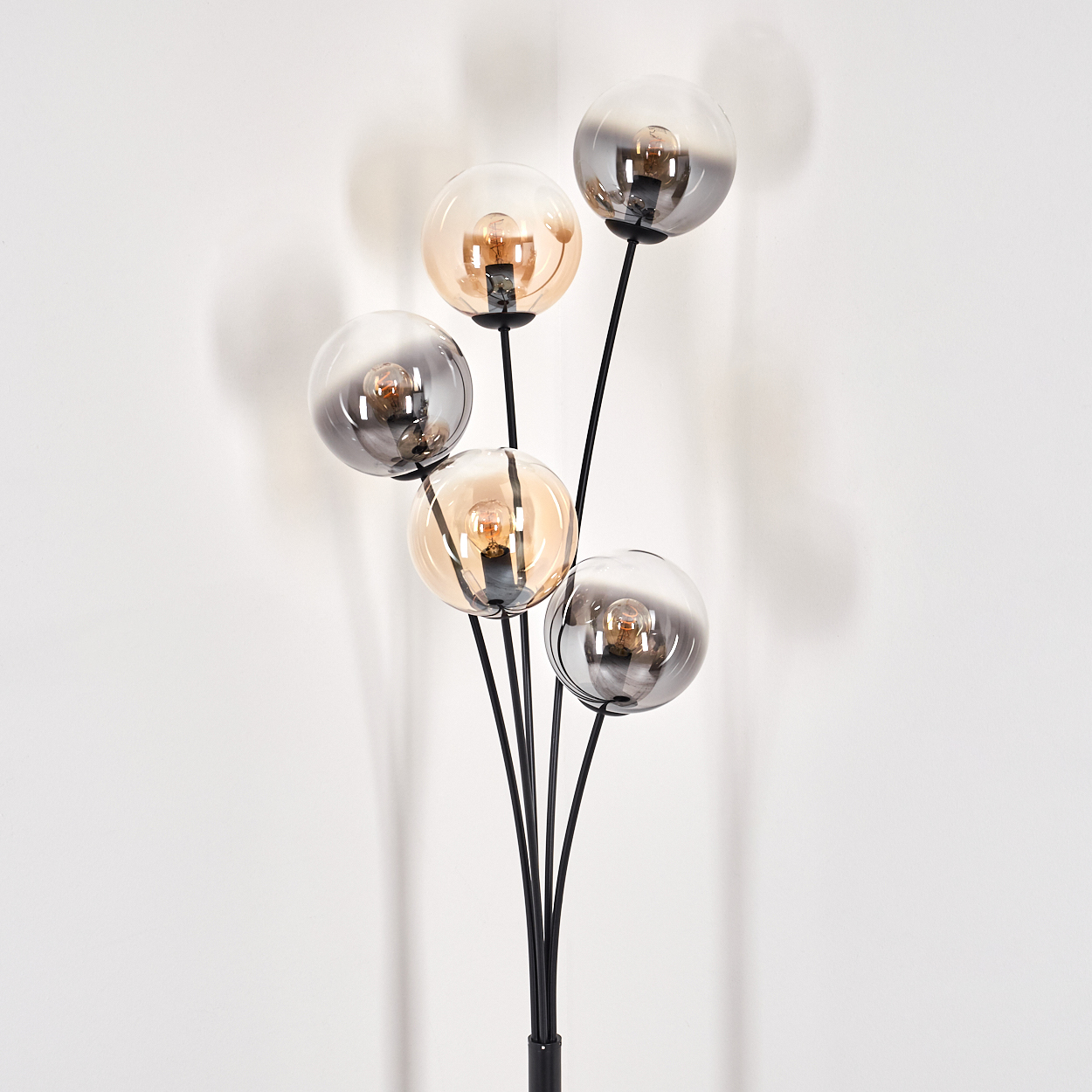 Nahaufnahme einer schwarzen Stehlampe mit fünf Kugelschirmen. Die Lampe hat ein modernes Design und steht vor einer weißen Wand.