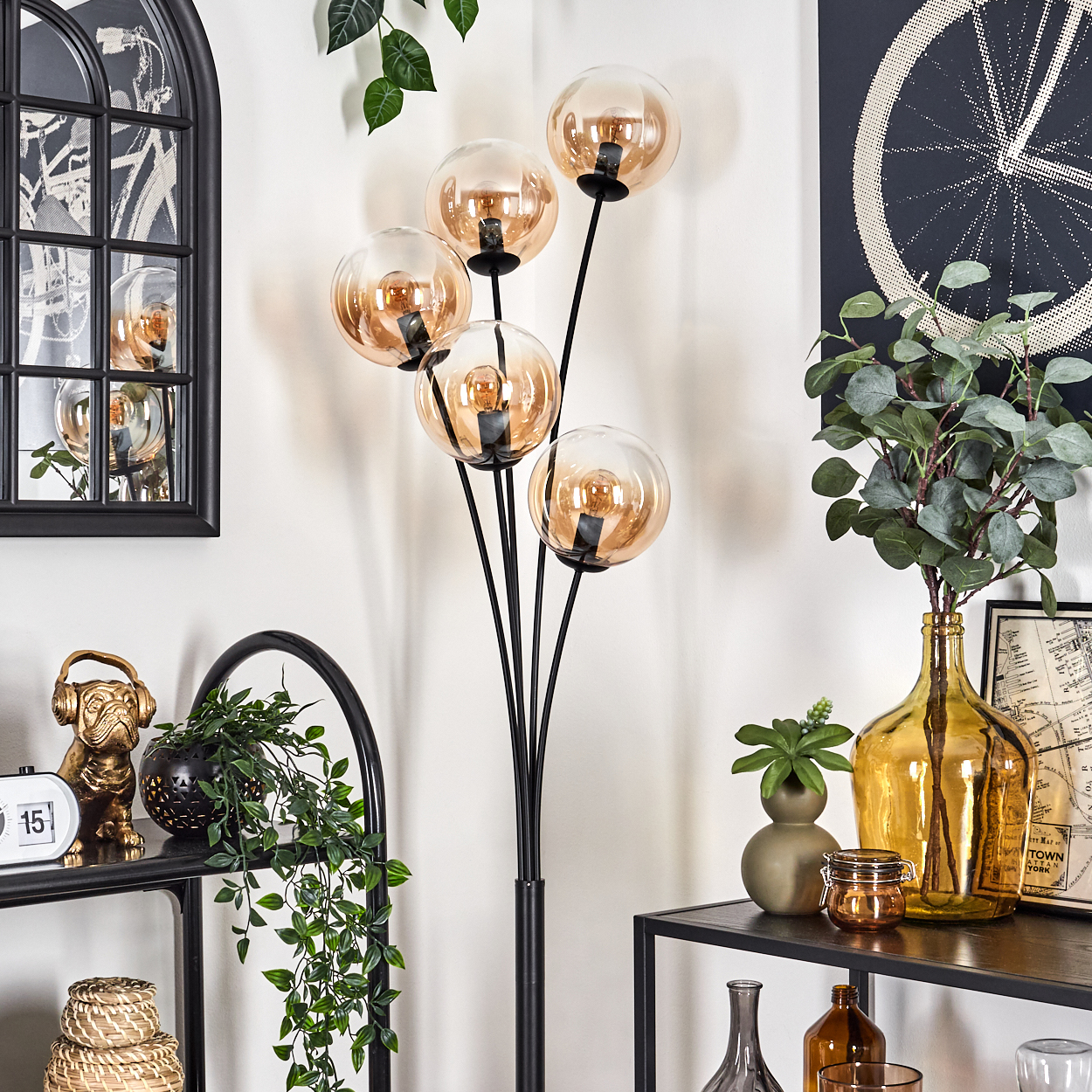Eine Zimmerecke mit einer schwarzen Stehlampe. Die Lampe hat Kugelschirme, und die Szene umfasst Regale und Dekoration.