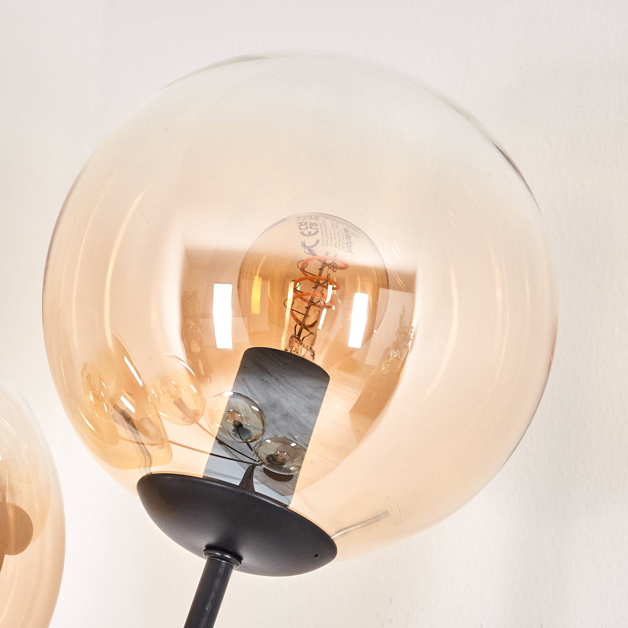 Nahaufnahme einer Glühbirne in einem orangefarbenen Glaskugelschirmen einer schwarzen Stehlampe.