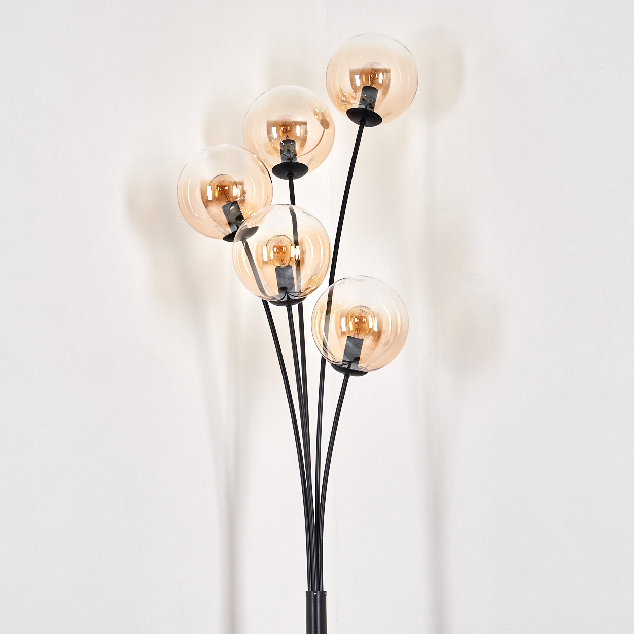 Schwarze Stehlampe mit bernsteinfarbenen Glaskugellampen. Weißer Wandhintergrund.