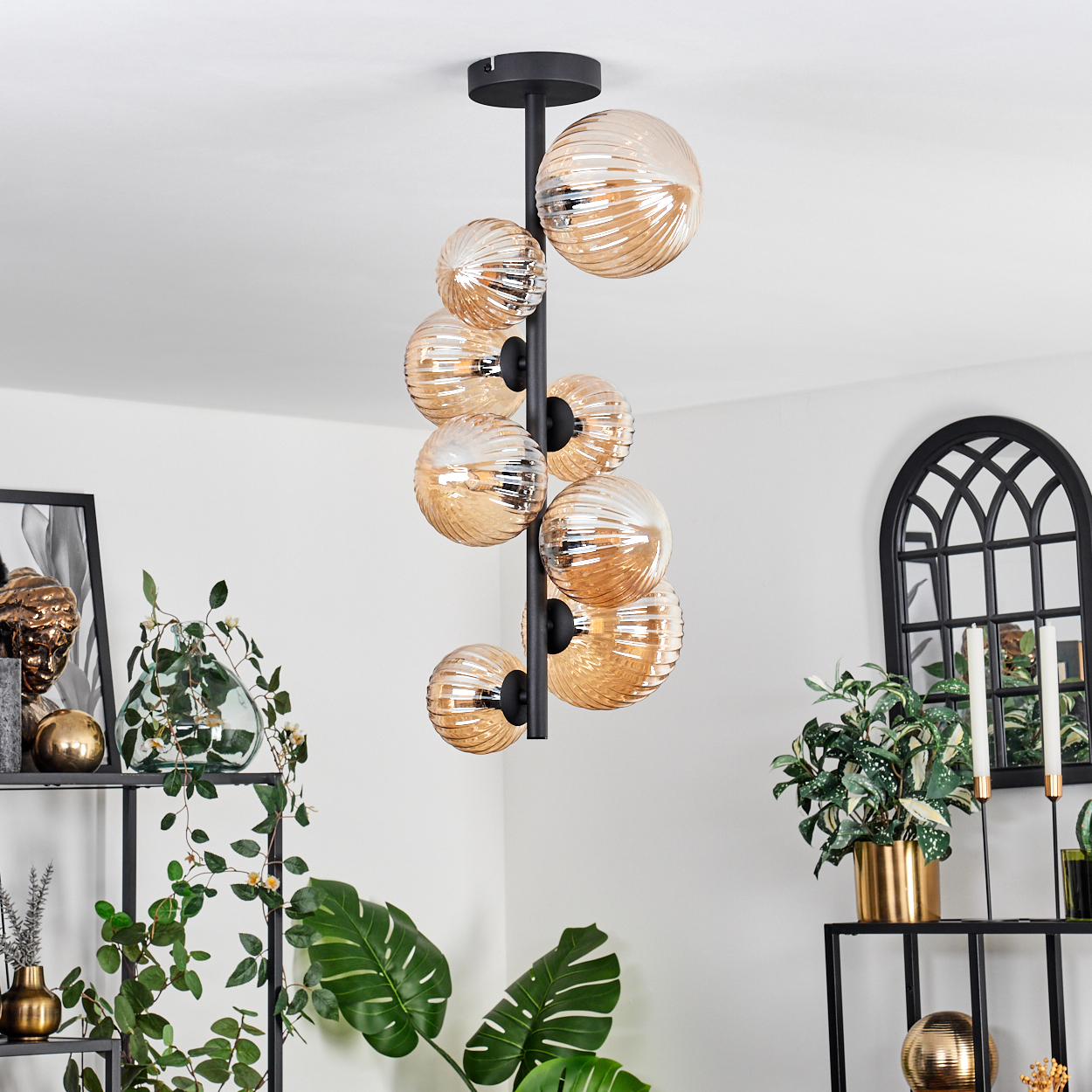 Deckenlampe in einer Raumeinstellung. Verfügt über bernsteinfarbene Glaskugeln und befindet sich in der Nähe von Pflanzen und Dekorationen.