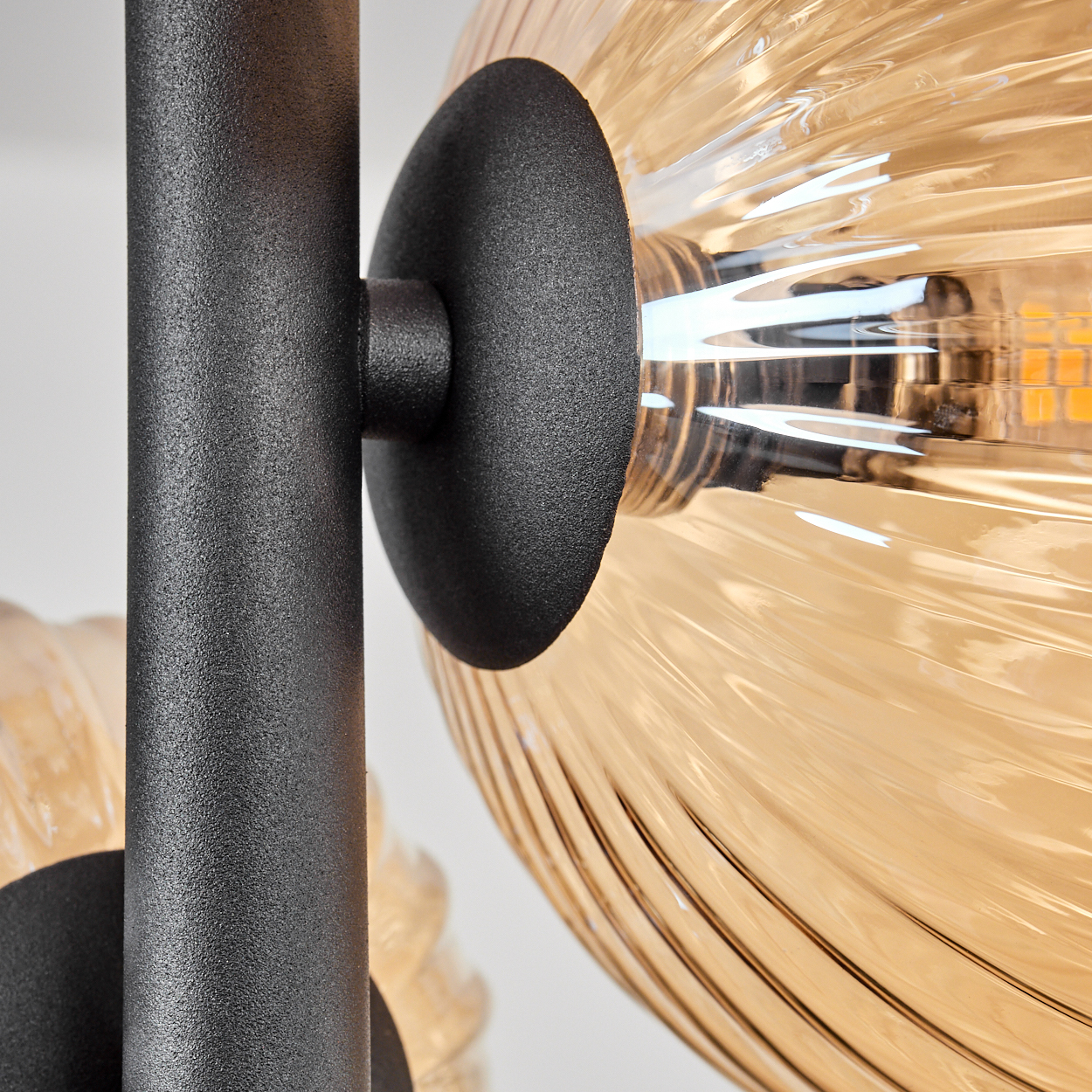 Nahaufnahme einer schwarzen Lampe mit einer klaren, bernsteinfarbenen Glaskugel. Im Inneren befindet sich eine helle Glühbirne. Der Hintergrund ist unscharf.