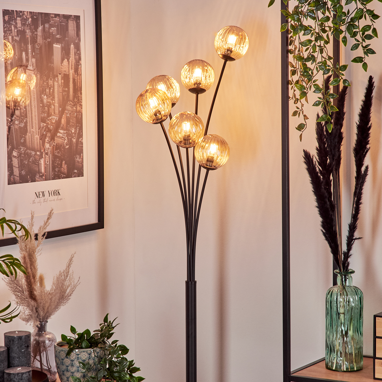 Eine Stehlampe mit bernsteinfarbenen Glaskugeln in einer Raumeinstellung. Die Lampe ist beleuchtet.