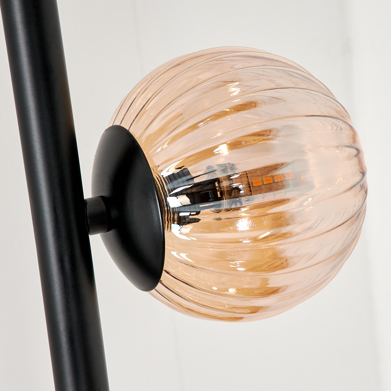 Nahaufnahme einer Glaskugellampe mit schwarzem Stiel. Die Lampe hat geripptes, bernsteinfarbenes Glas.