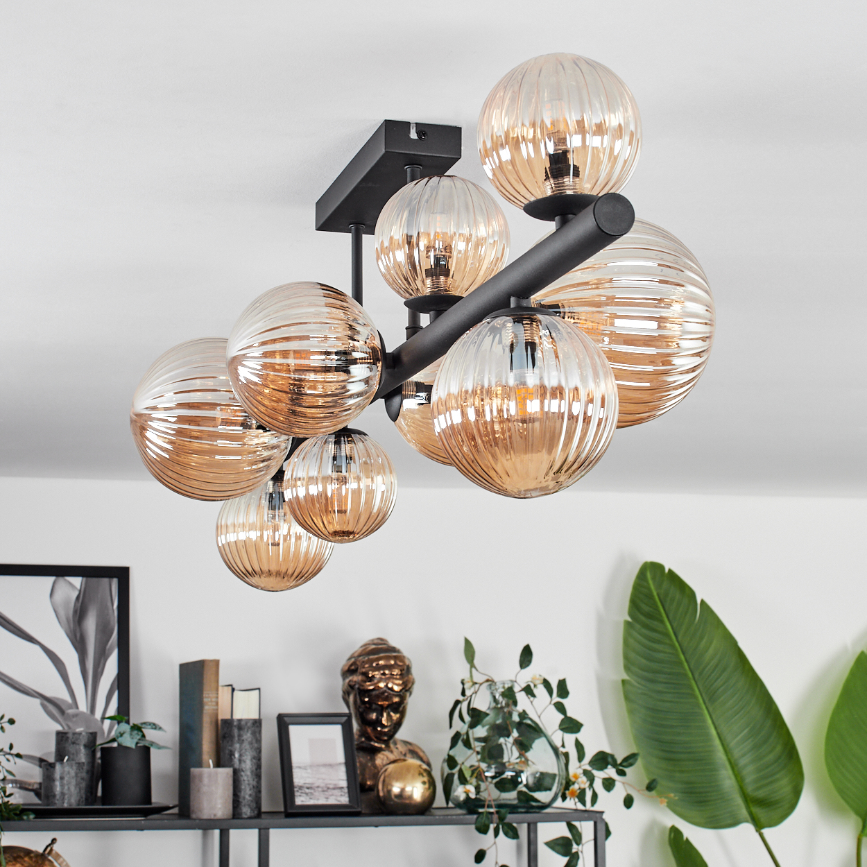 Eine Deckenlampe mit neun bernsteinfarbenen Glaskugeln. Die Lampe ist an einer schwarzen Stange befestigt. Bücher und Deko sichtbar.