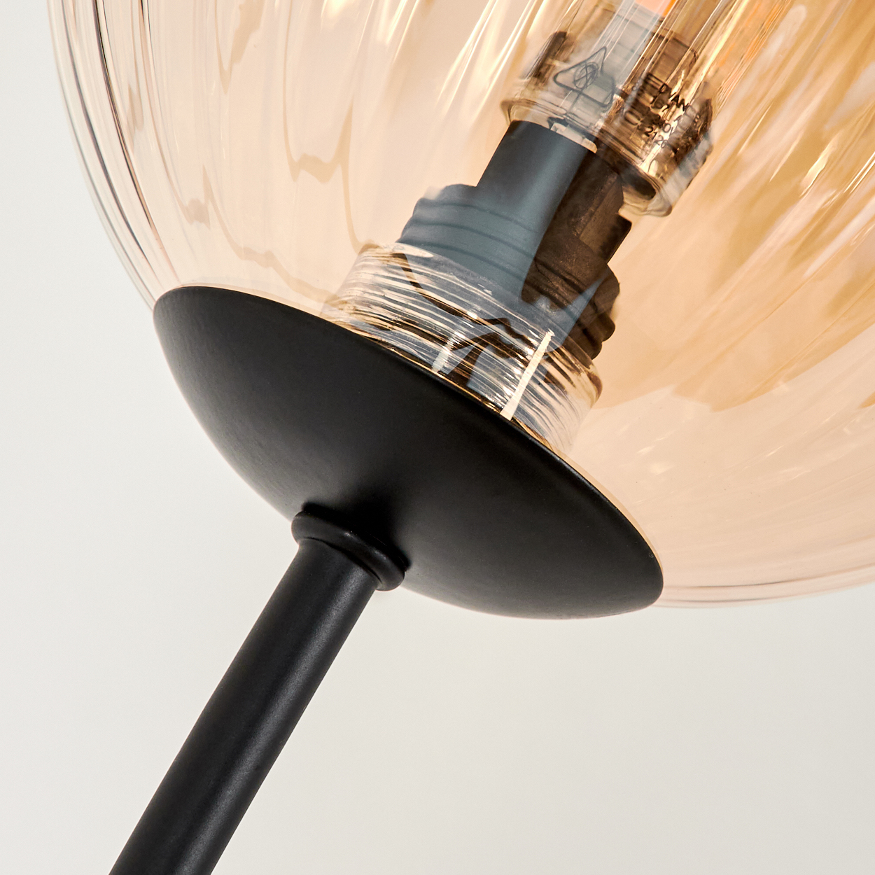Nahaufnahme eines schwarzen Metalllampenstiels, der eine bernsteinfarbene Glaskugel mit eingesetzter Glühbirne hält.