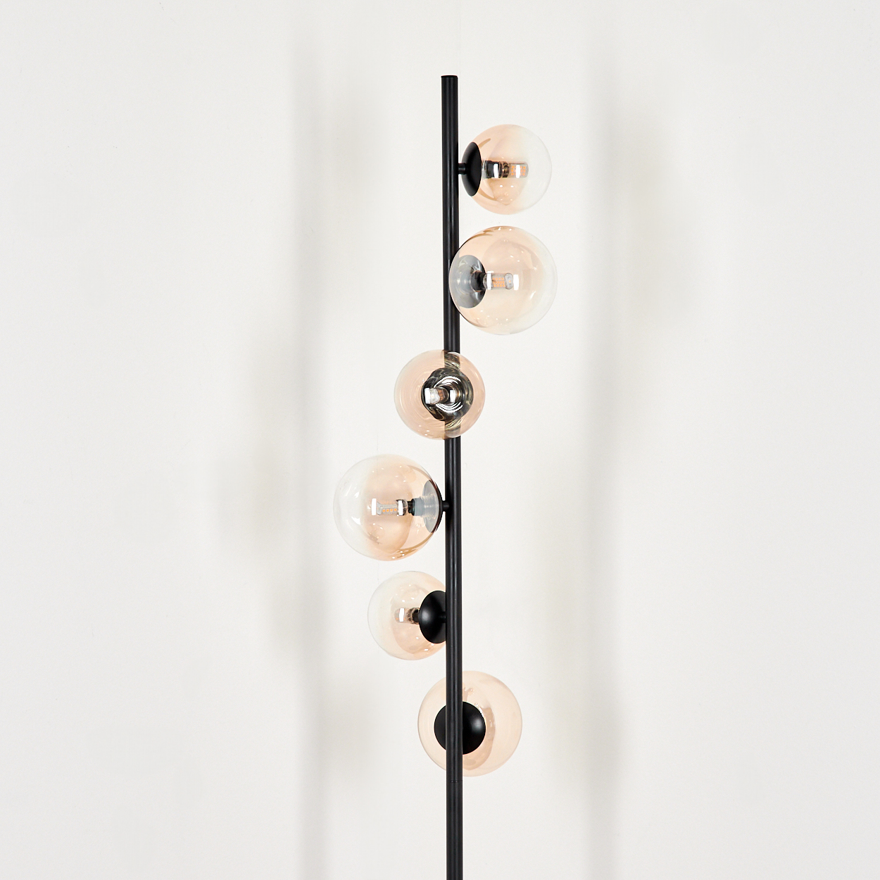 Hohe Stehlampe mit bernsteinfarbenen Kugeln, schwarzer Stange. Schlichtes Design vor weißem Hintergrund.