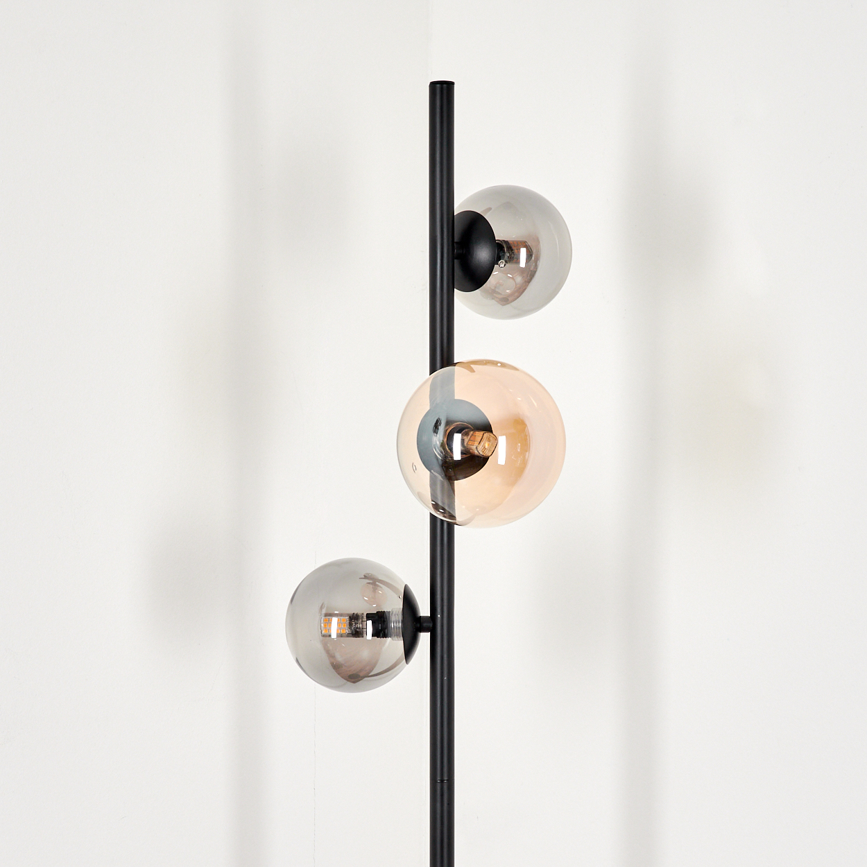 Nahaufnahme des oberen Teils einer schwarzen Stehlampe mit drei Glaskugeln.