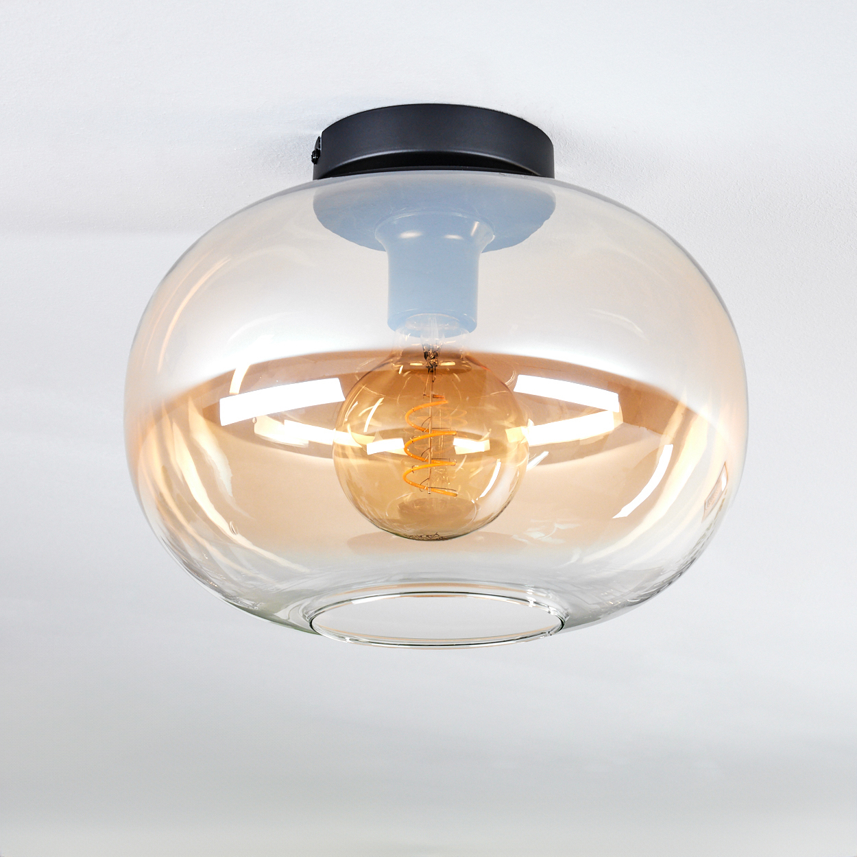 Deckenlampe mit Glasschirm und sichtbarer Glühbirne. Die Glühbirne ist golden.