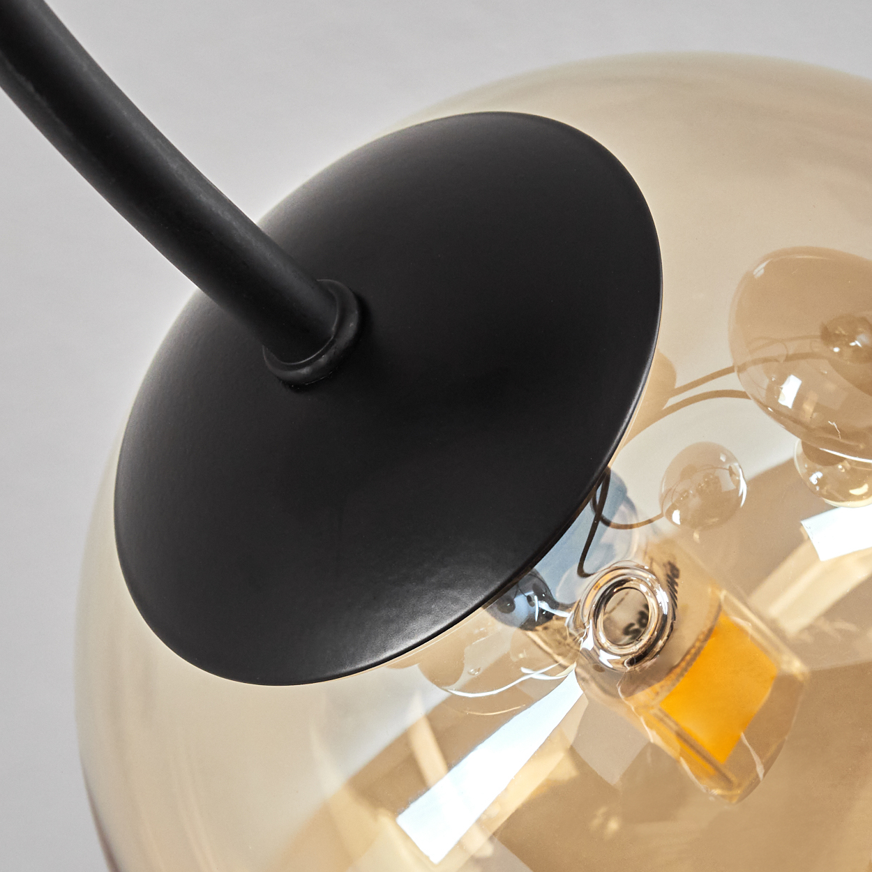 Nahaufnahme einer Deckenlampe mit schwarzem Sockel und goldener, kugelförmiger Glühbirne.