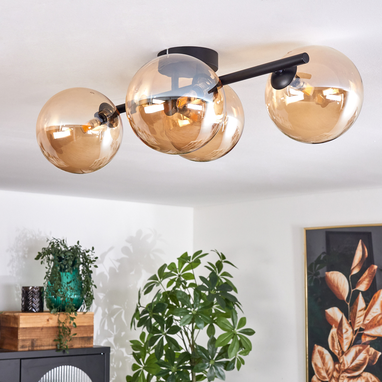 Deckenlampe mit vier goldenen, kugelförmigen Lichtern und einem schwarzen Arm. Der Hintergrund hat Pflanzen und Möbel.