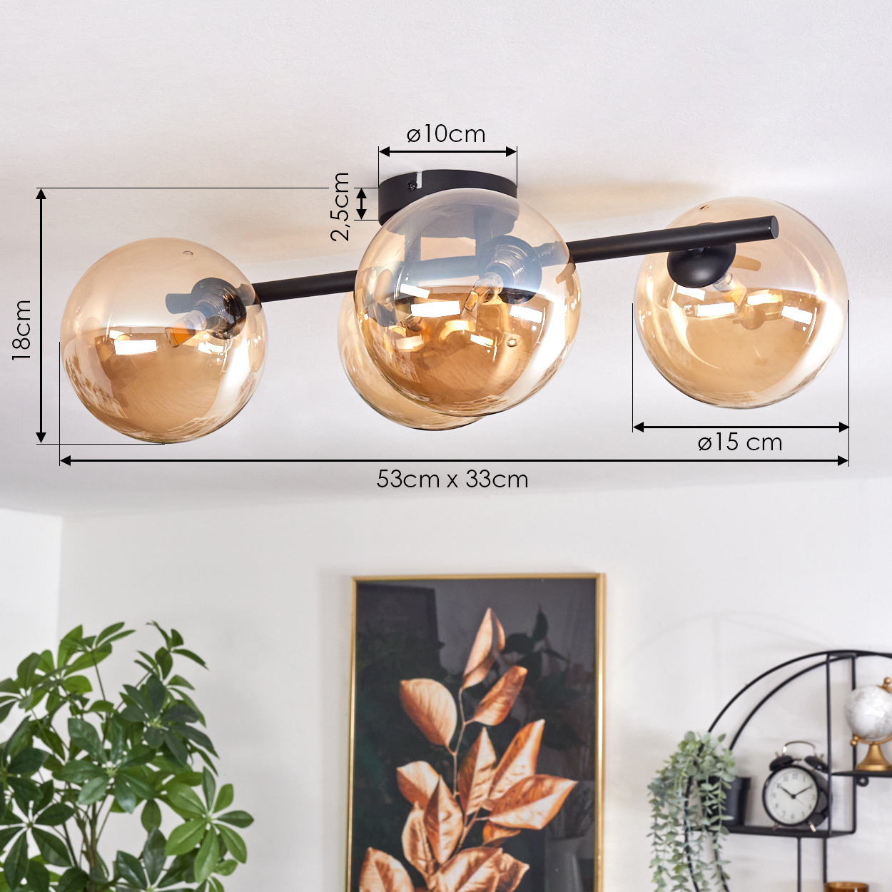 Deckenlampe mit drei goldenen, kugelförmigen Lichtern. Der Hintergrund zeigt Pflanzen und Dekorationen.