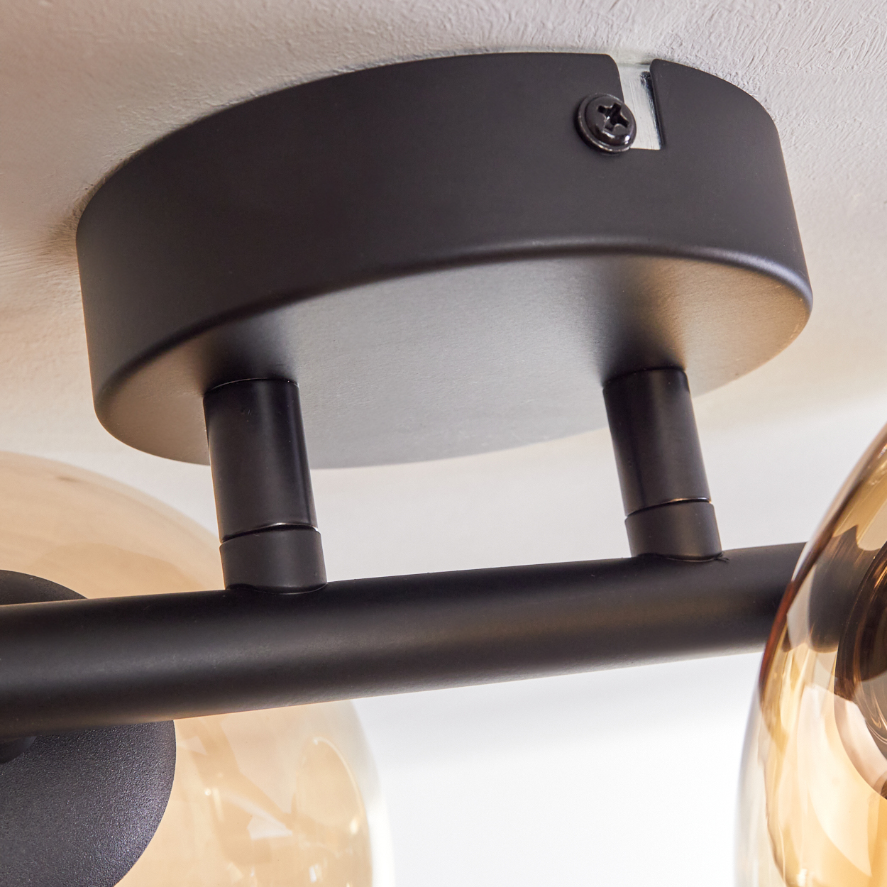 Nahaufnahme des schwarzen Sockels einer Deckenlampe und der Verbindung mit den Armen der Lampe.