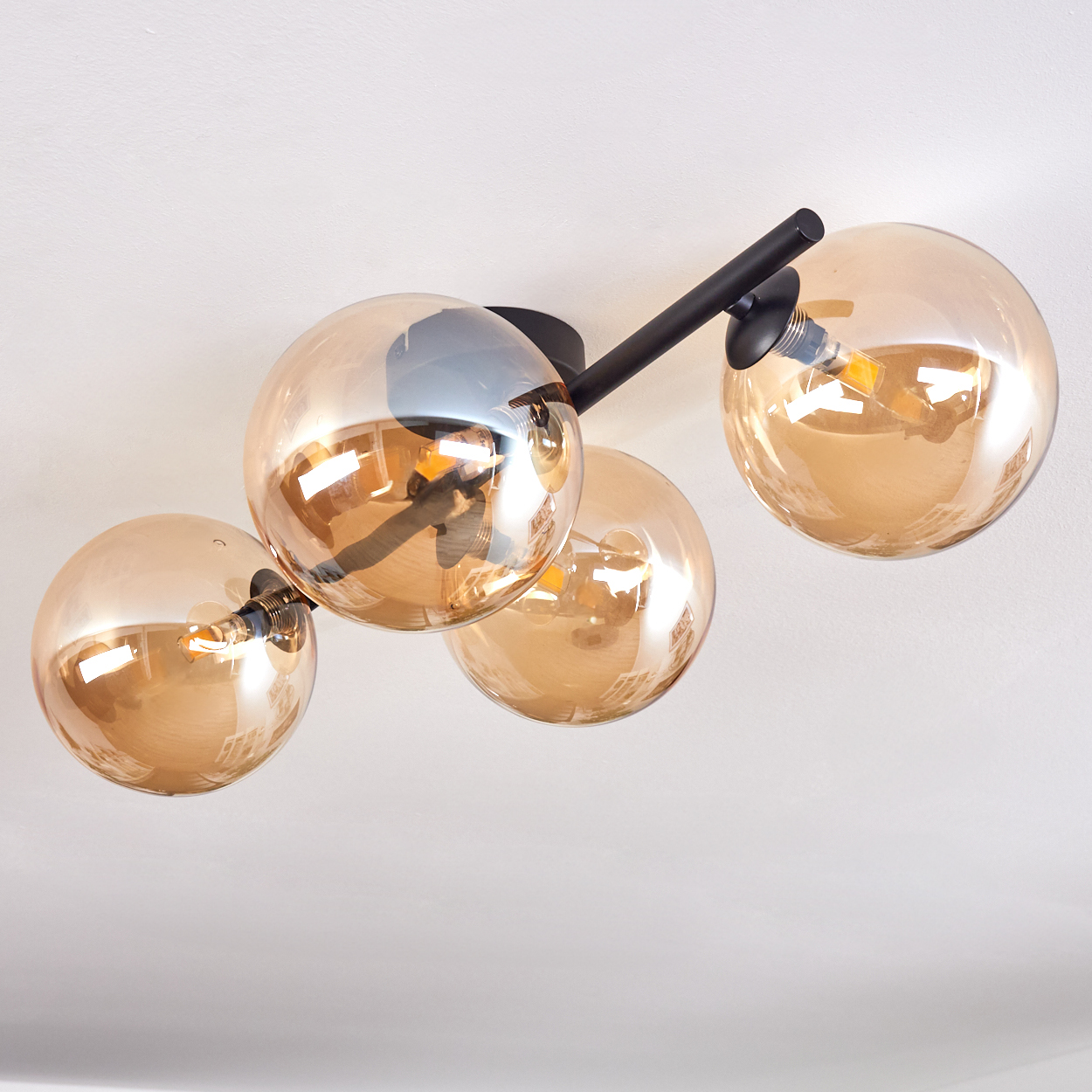 Deckenlampe mit vier goldenen, kugelförmigen Lichtern und schwarzen Armen. Die Glühbirnen sind sichtbar.