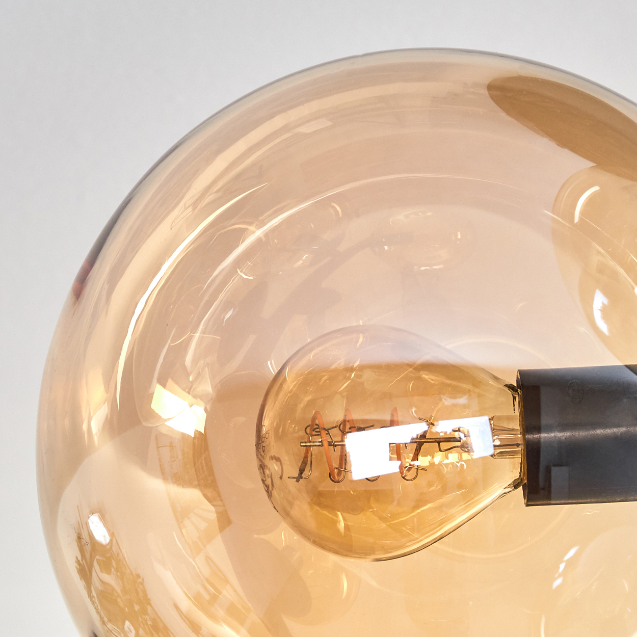 Nahaufnahme einer Glühbirne in einer Glaskugel mit goldenem Farbton auf weißem Hintergrund.