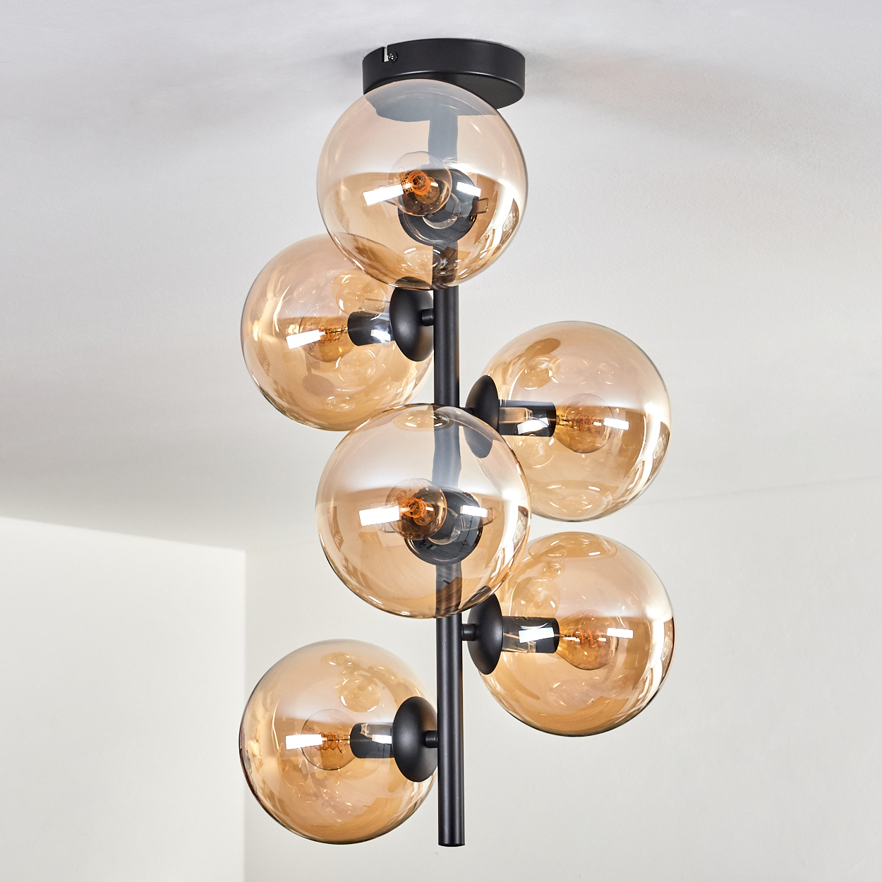 Eine Deckenlampe mit sechs bernsteinfarbenen Glaskugeln, vertikal angeordnet. Das Licht ist an.