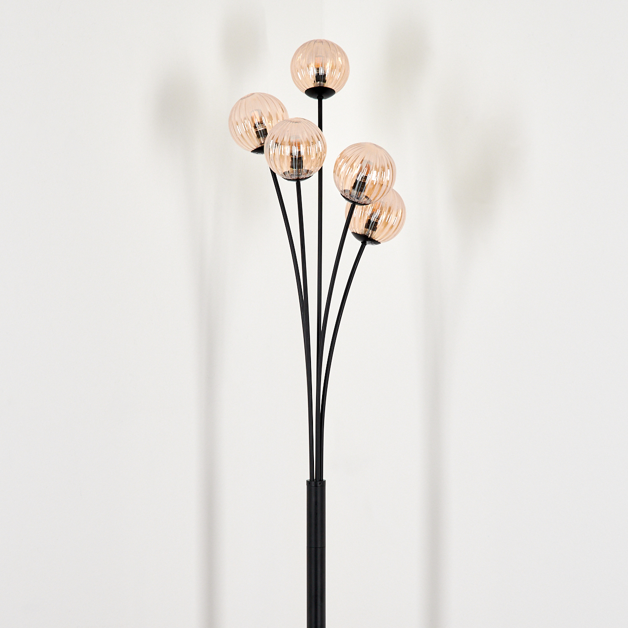 Stehlampe mit schwarzem Stiel und fünf bernsteinfarbenen Glaskugeln, vor weißer Wand.