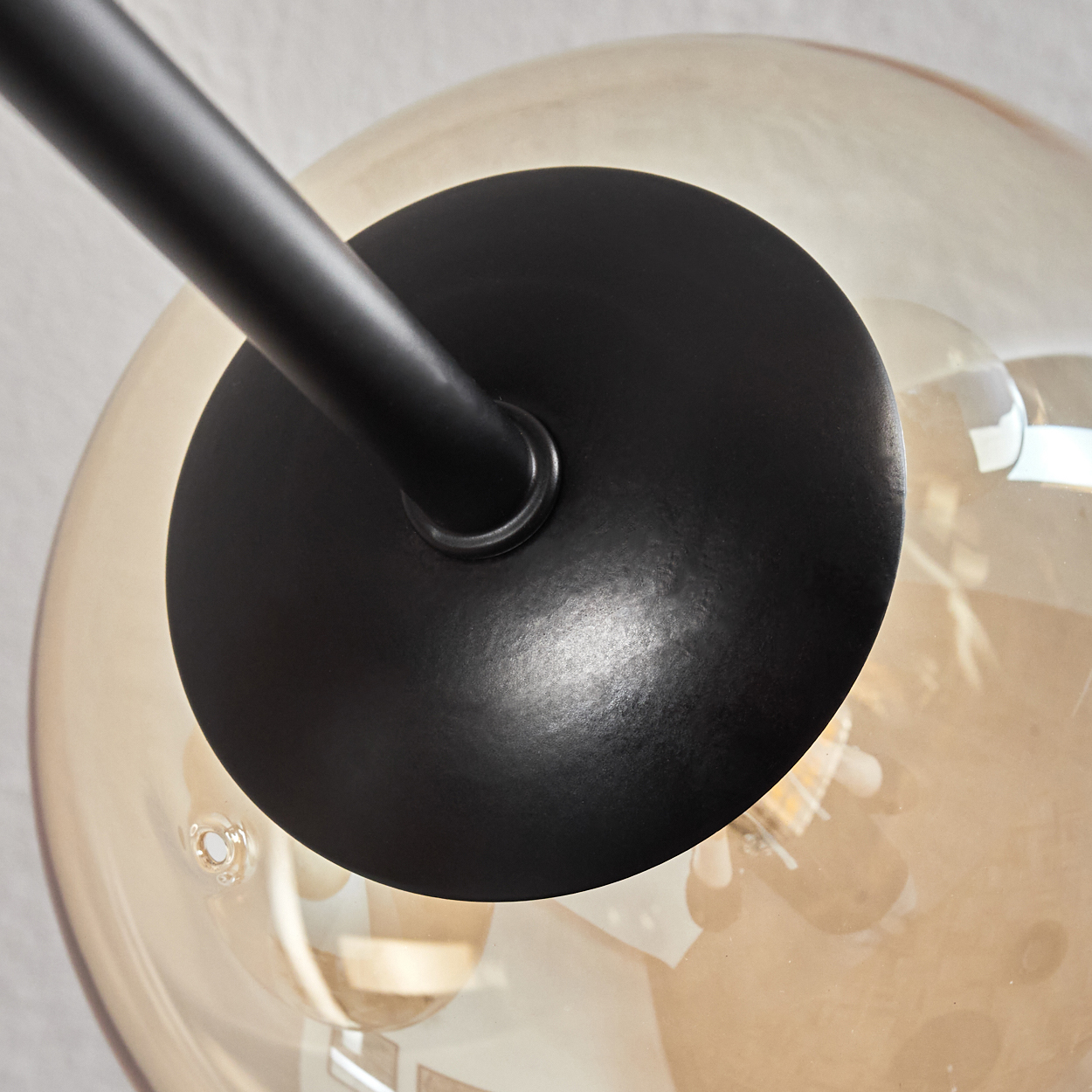 Nahaufnahme von schwarzem Metallträger und bernsteinfarbener Glaskugel, mit Glühbirne innen.