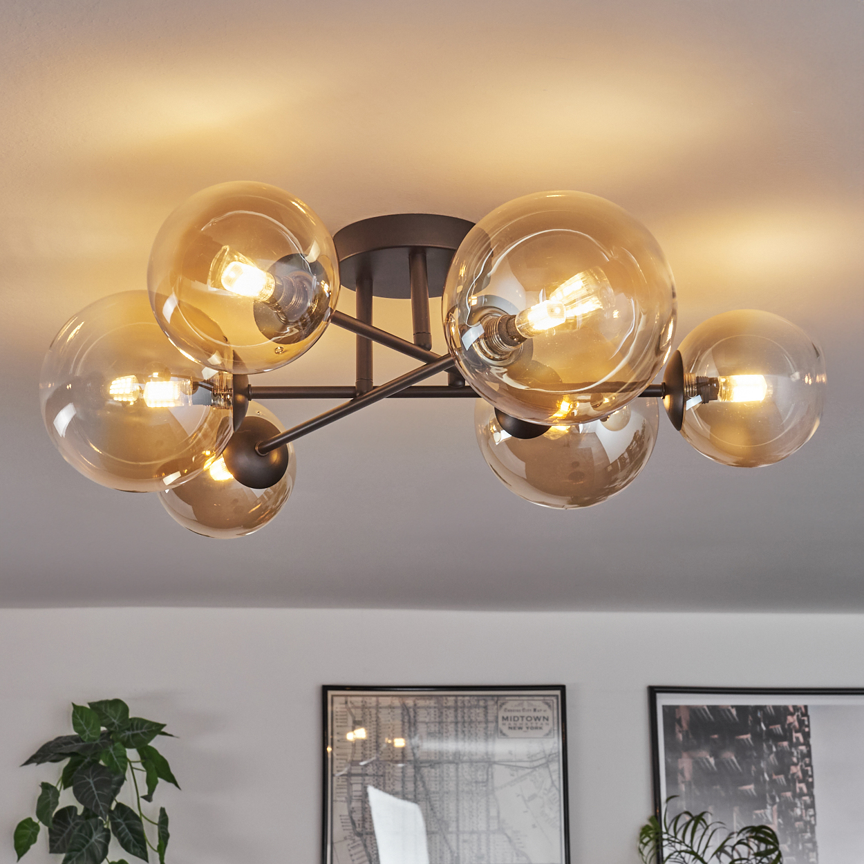 Deckenleuchte mit sechs bernsteinfarbenen Glaskugeln, schwarzem Metallrahmen, hellen Glühbirnen und weißer Decke.