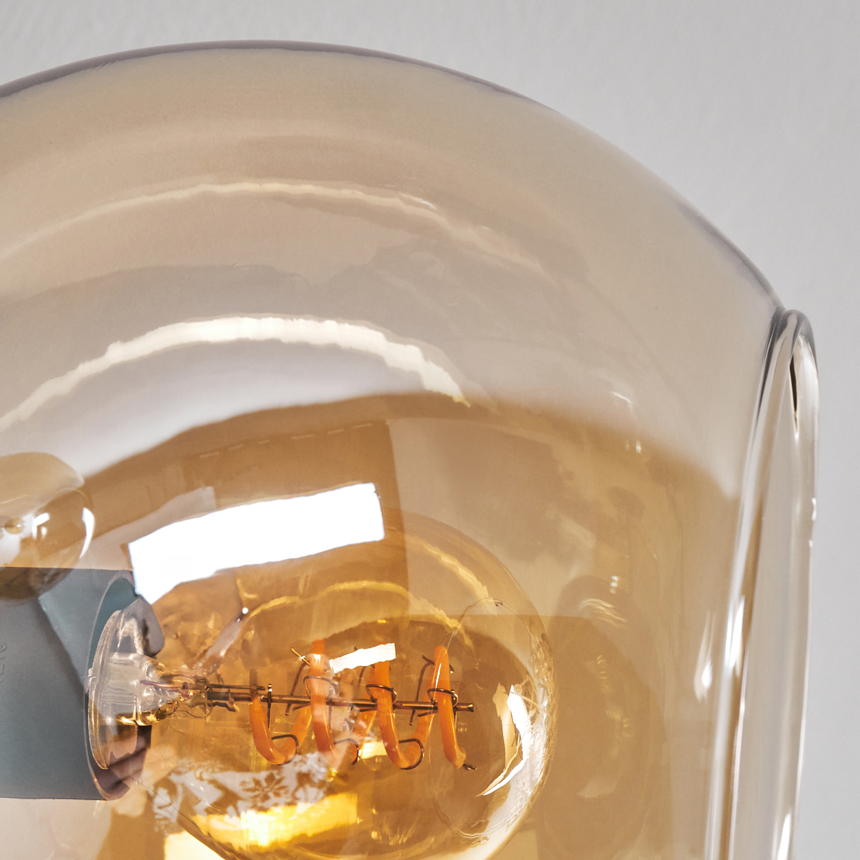 Nahaufnahme einer bernsteinfarbenen Glaskugel, mit einer sichtbaren Glühbirne im Inneren. Das Glas hat eine leichte Bernsteinfärbung.