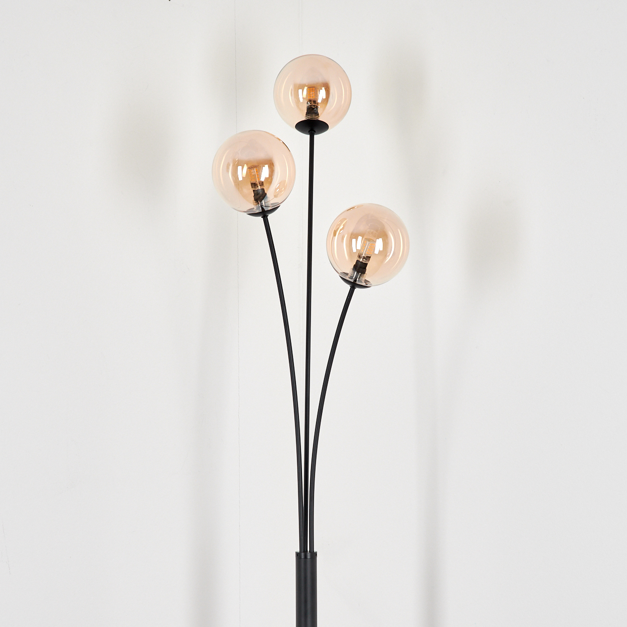 Stehlampe mit drei bernsteinfarbenen Glaskugeln. Weißer Hintergrund.
