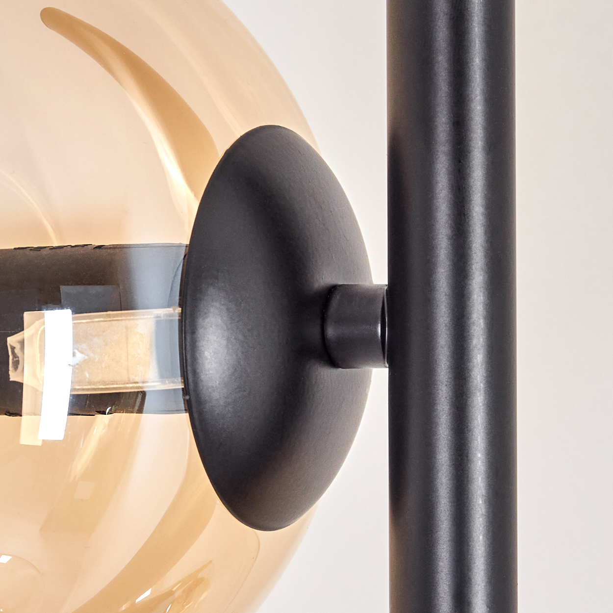 Nahaufnahme einer schwarzen Metallleuchte, die einen bernsteinfarbenen Glaskolben hält, auf weißem Hintergrund.