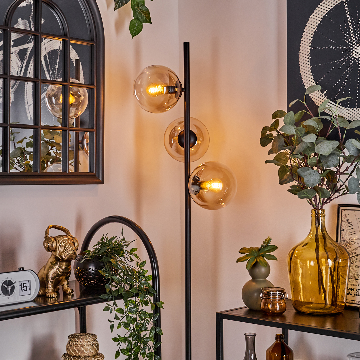 Schwarze Stehlampe mit drei bernsteinfarbenen Kugeln, Dekorationsgegenständen und einem Spiegel an der Wand.