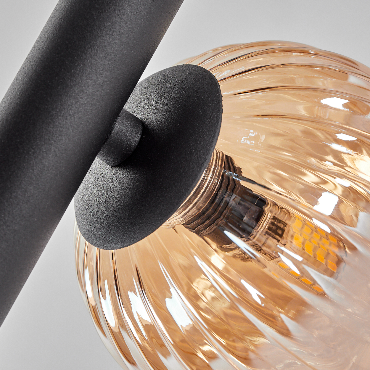 Nahaufnahme einer Lampe. Bernsteinfarbene Glaskugel an einem schwarzen Metallträger befestigt.