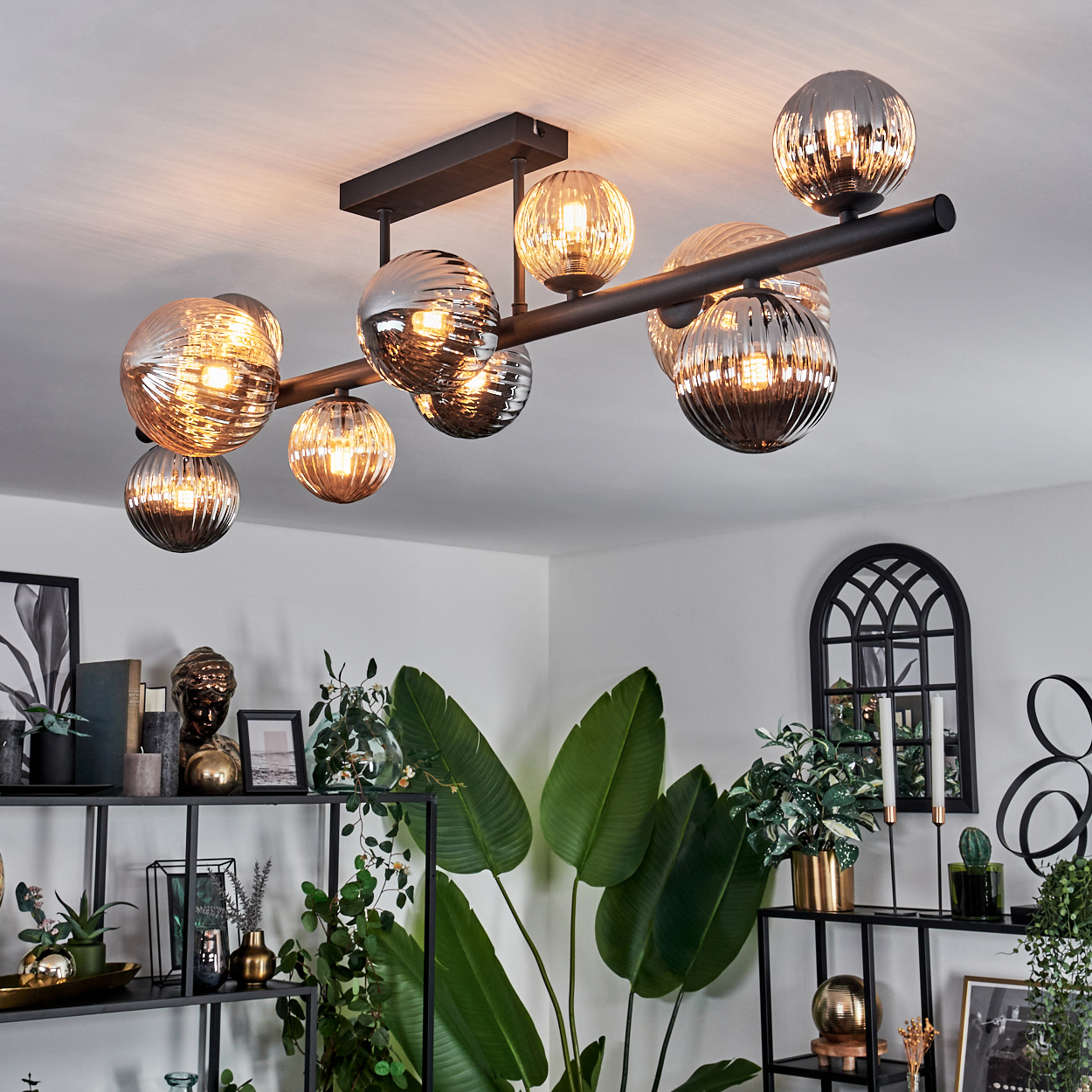 Eine Deckenlampe mit mehreren kugelförmigen Glaslampen in einem Wohnzimmer mit Pflanzen.