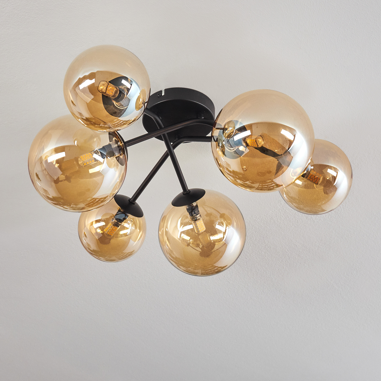 Deckenlampe mit bernsteinfarbenen Glaskugeln und leuchtenden Glühbirnen, vor weißem Deckenhintergrund.