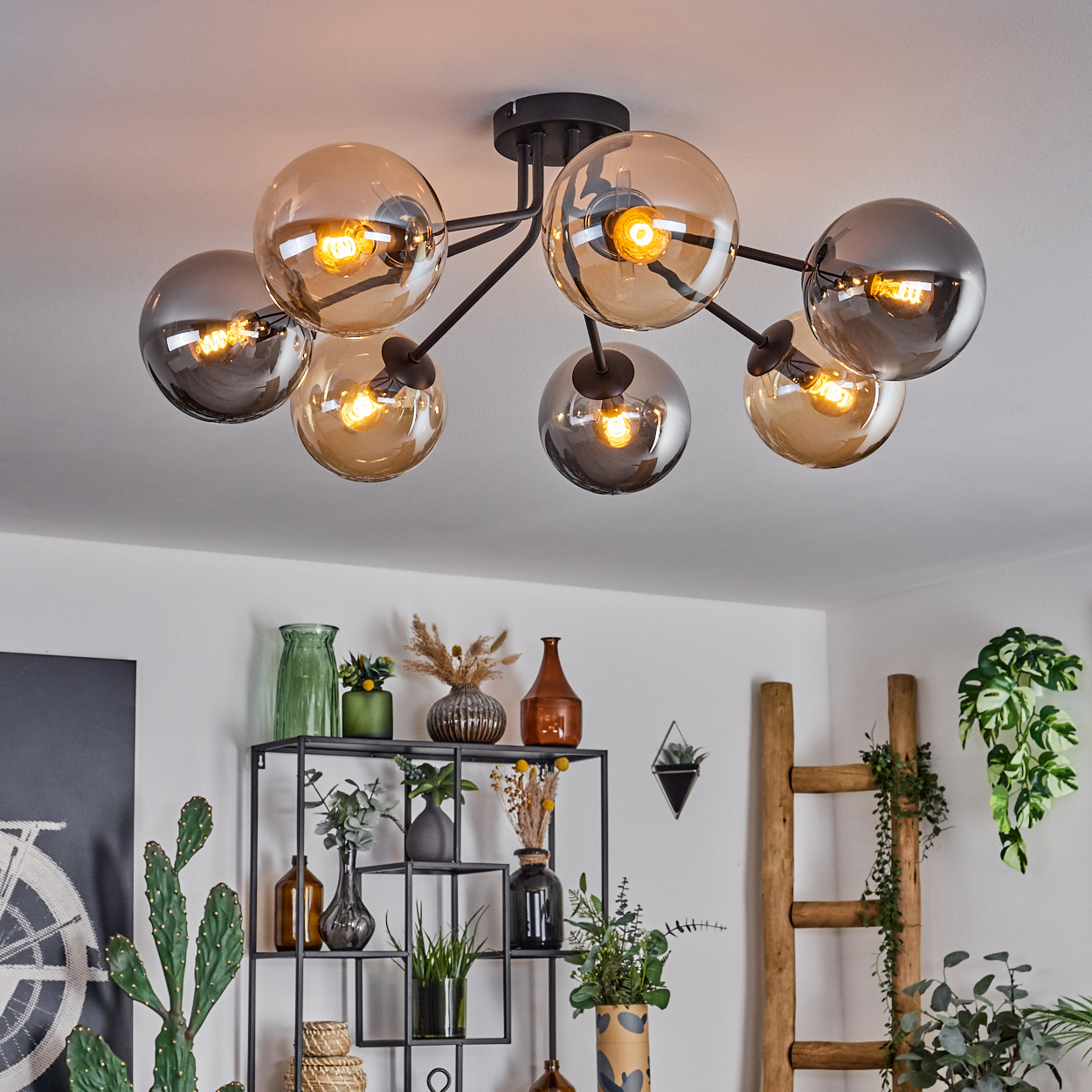 Schwarze Deckenlampe mit bernsteinfarbenen und grauen Glaskugeln, die einen Raum mit Pflanzen und Heimdekor beleuchtet.