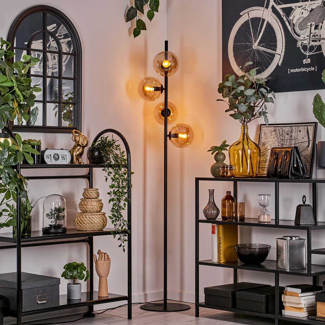 Stehlampe mit bernsteinfarbenen Kugeln, Dekor auf schwarzen Regalen und einem Fahrrad-Kunstdruck im Hintergrund.