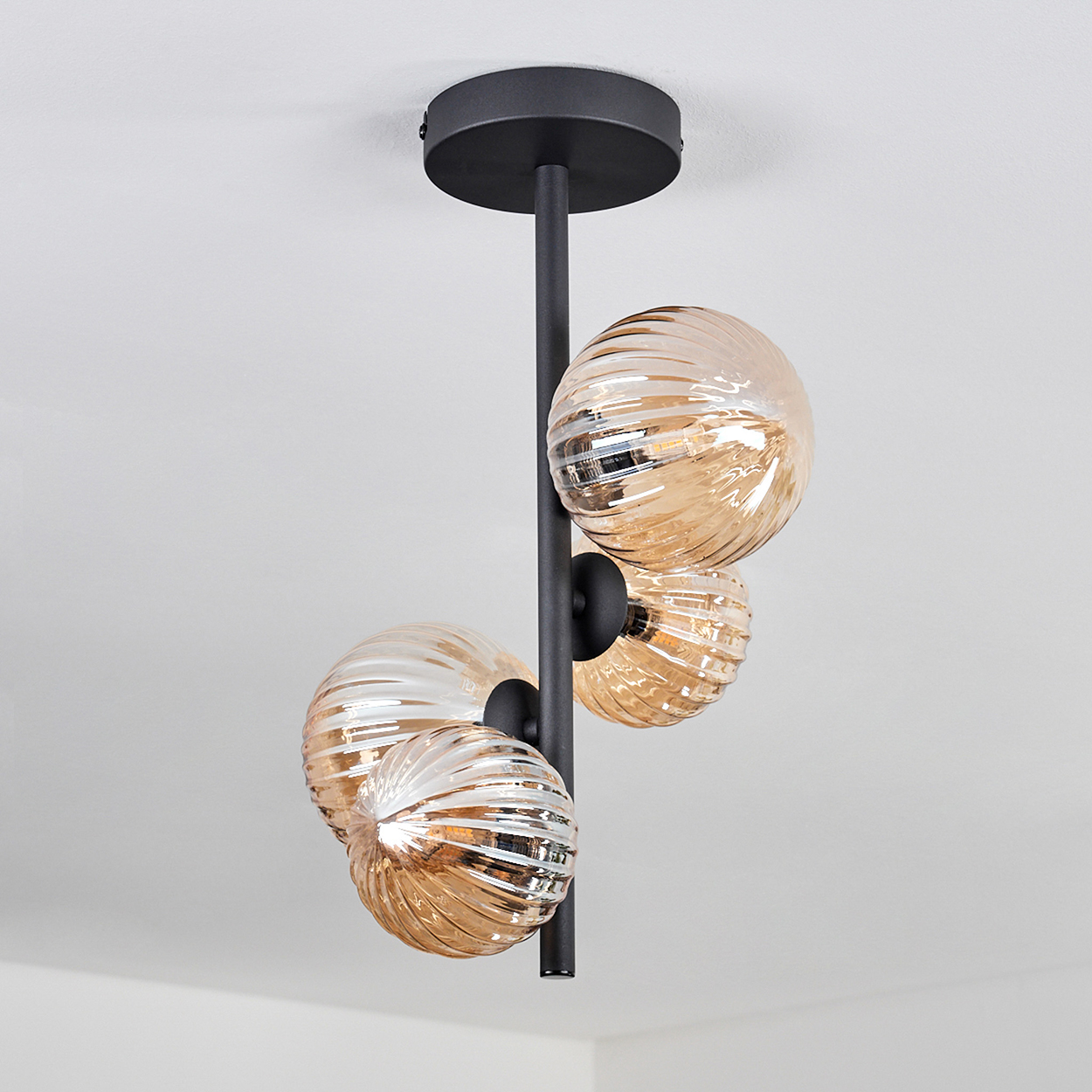 Drei kugelförmige Leuchten hängen von einer Decke. Die Leuchten haben bernsteinfarbenes Glas und schwarze Stiele.