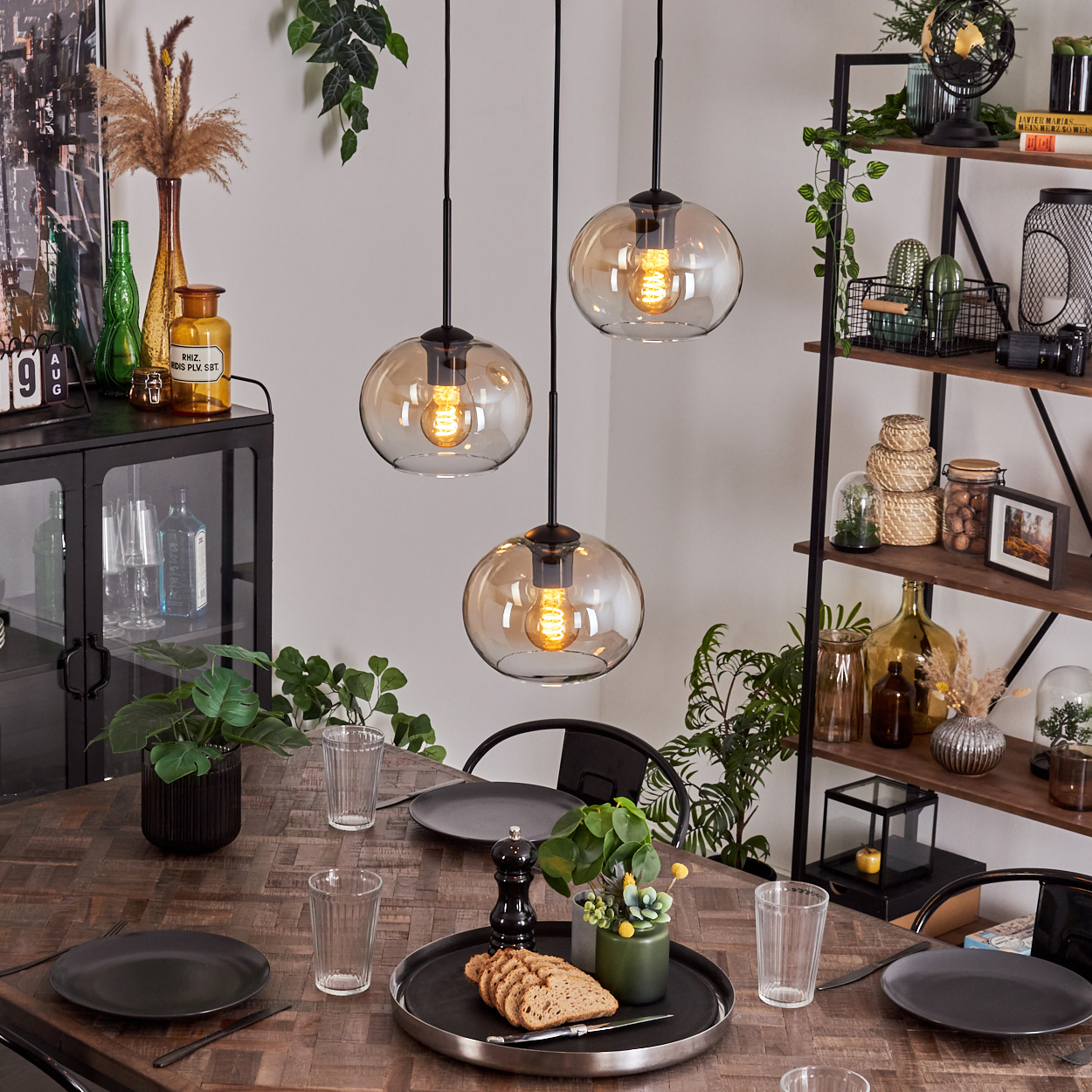 Esszimmer mit Hängelampen, Tisch und Dekoration. Die Lampen sind kugelförmig mit warmen Glühbirnen.