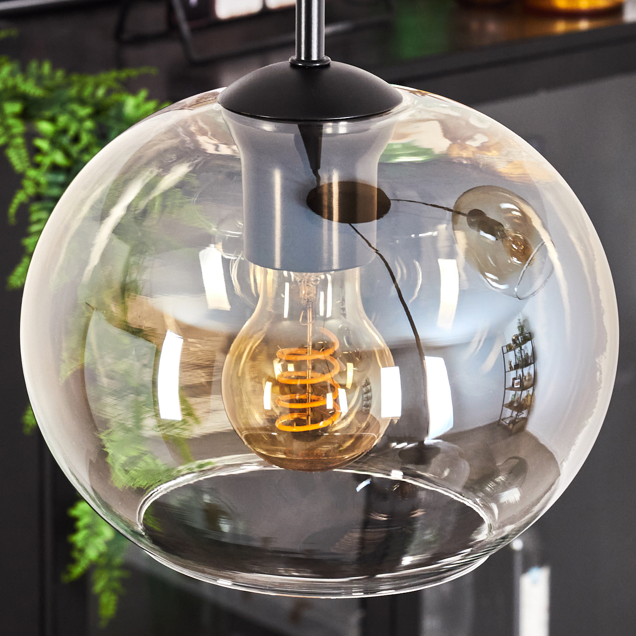 Nahaufnahme einer Pendelleuchte mit großem bernsteinfarbenem Glasschirm mit Edison-Glühbirne, schwarze Halterung, schwarzer Hintergrund.