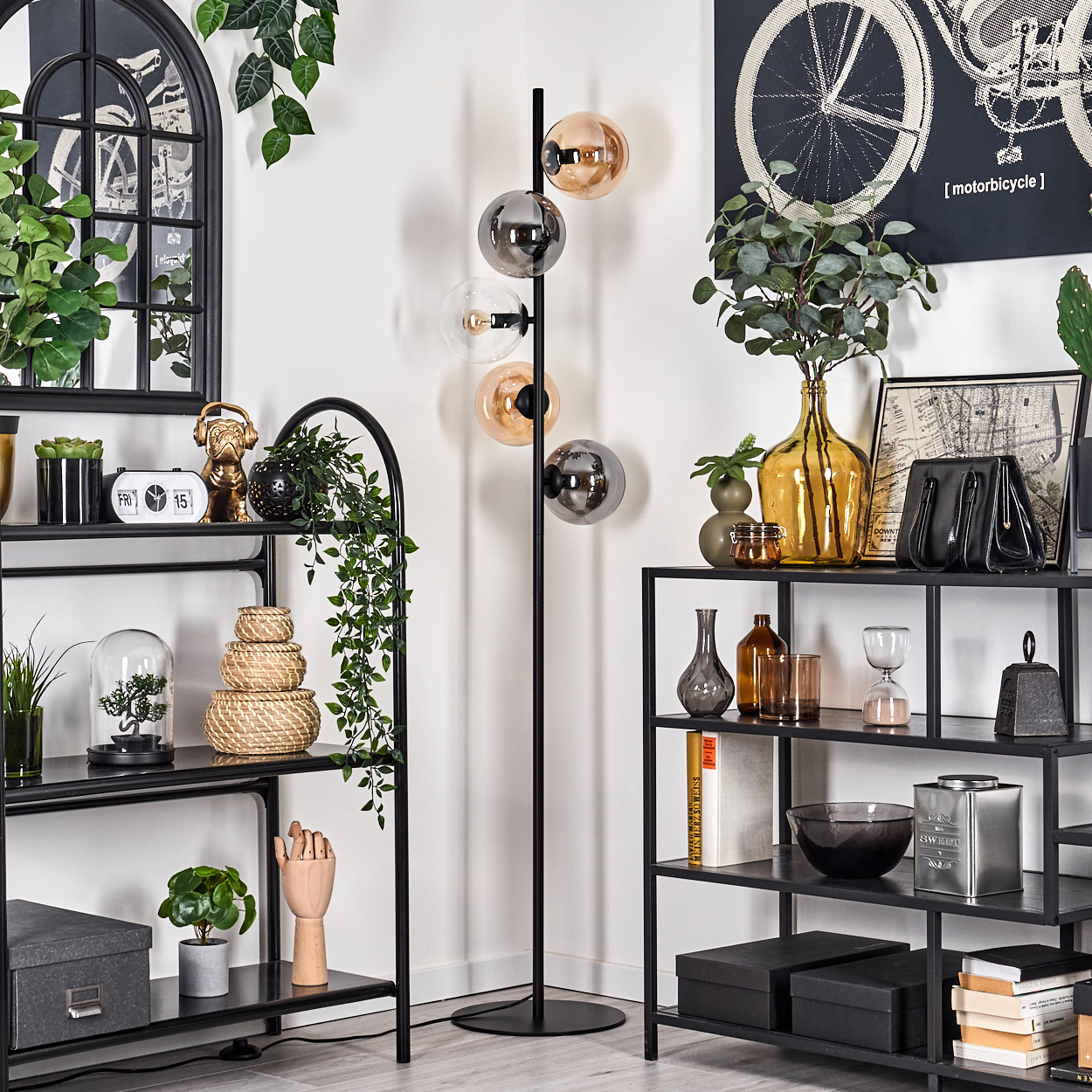 Wohnzimmer mit Stehlampe und verschiedenen Dekorationen. Regale, Kunstwerke und Pflanzen sind vorhanden.