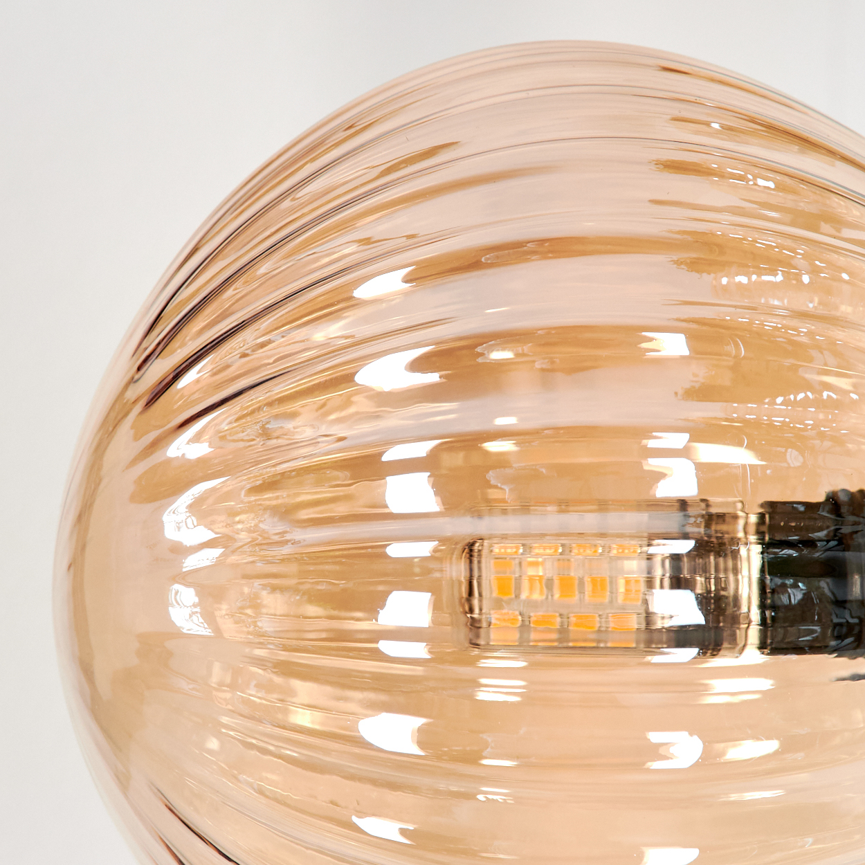 Nahaufnahme einer bernsteinfarbenen Glaskugel-Lampe mit geripptem Design, die die Glühbirne zeigt.