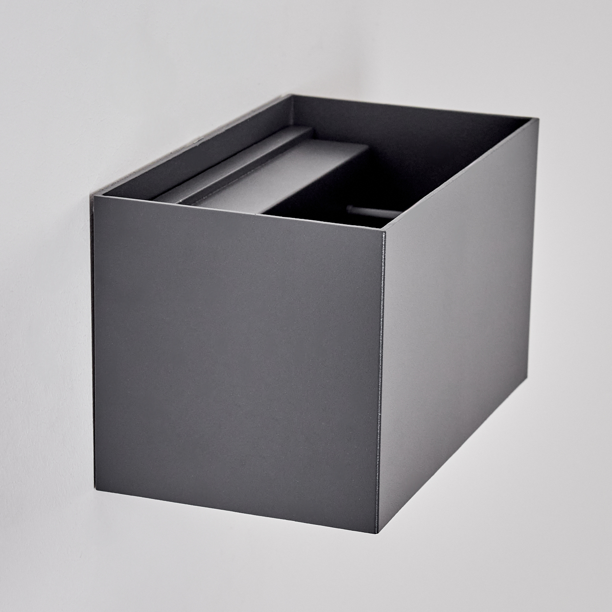 Graue rechteckige Box an einer weißen Wand montiert, mit offener Oberseite und Innenstruktur.