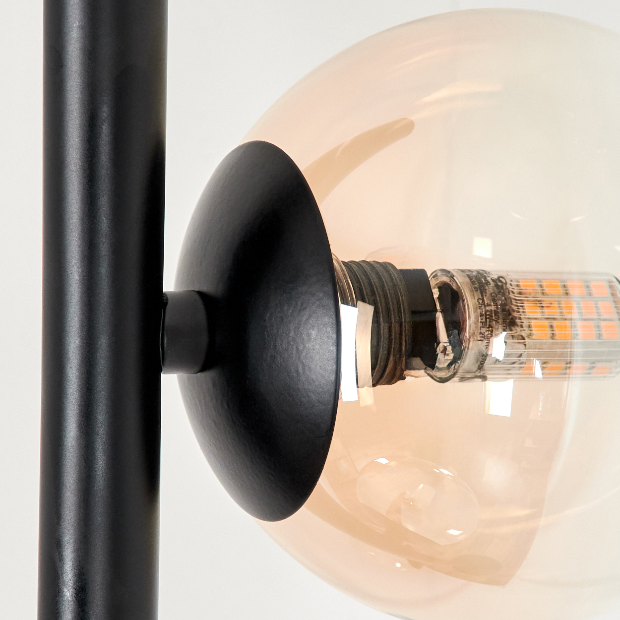 Nahaufnahme einer Lampenkugel. Bernsteinfarbene Glaskugel mit LED-Innenbeleuchtung. Schwarzes Metall.