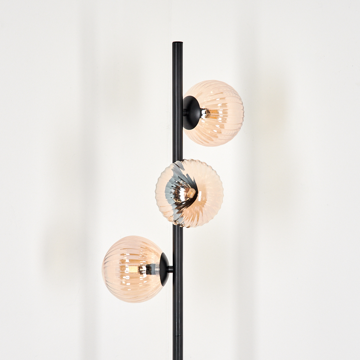 Stehlampe mit gerippten, bernsteinfarbenen Kugeln. Modernes Design vor weißer Wand.