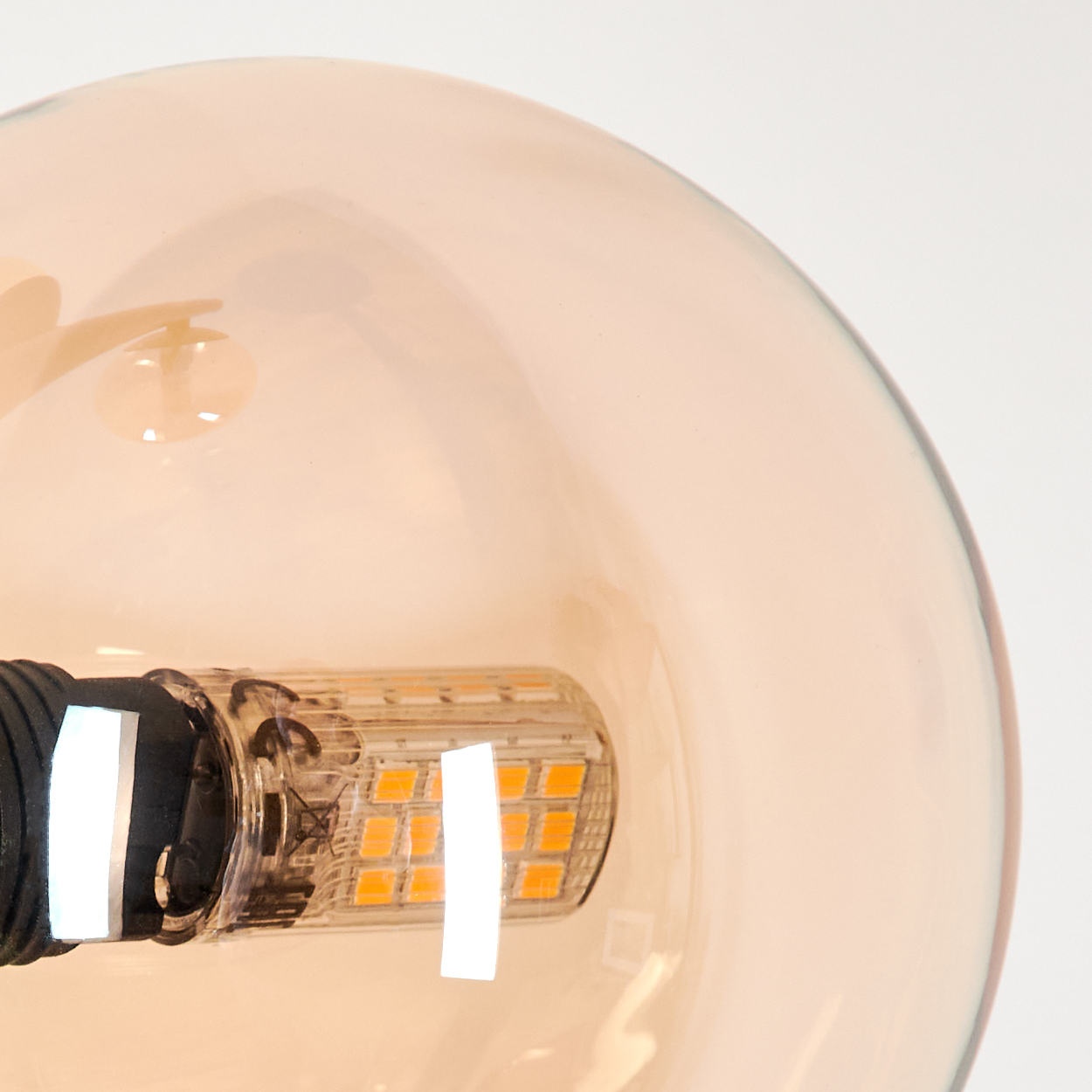 Nahaufnahme einer Lampenkugel. Bernsteinfarbenes Glas mit LED-Licht. Schwarzer Metallhalter.