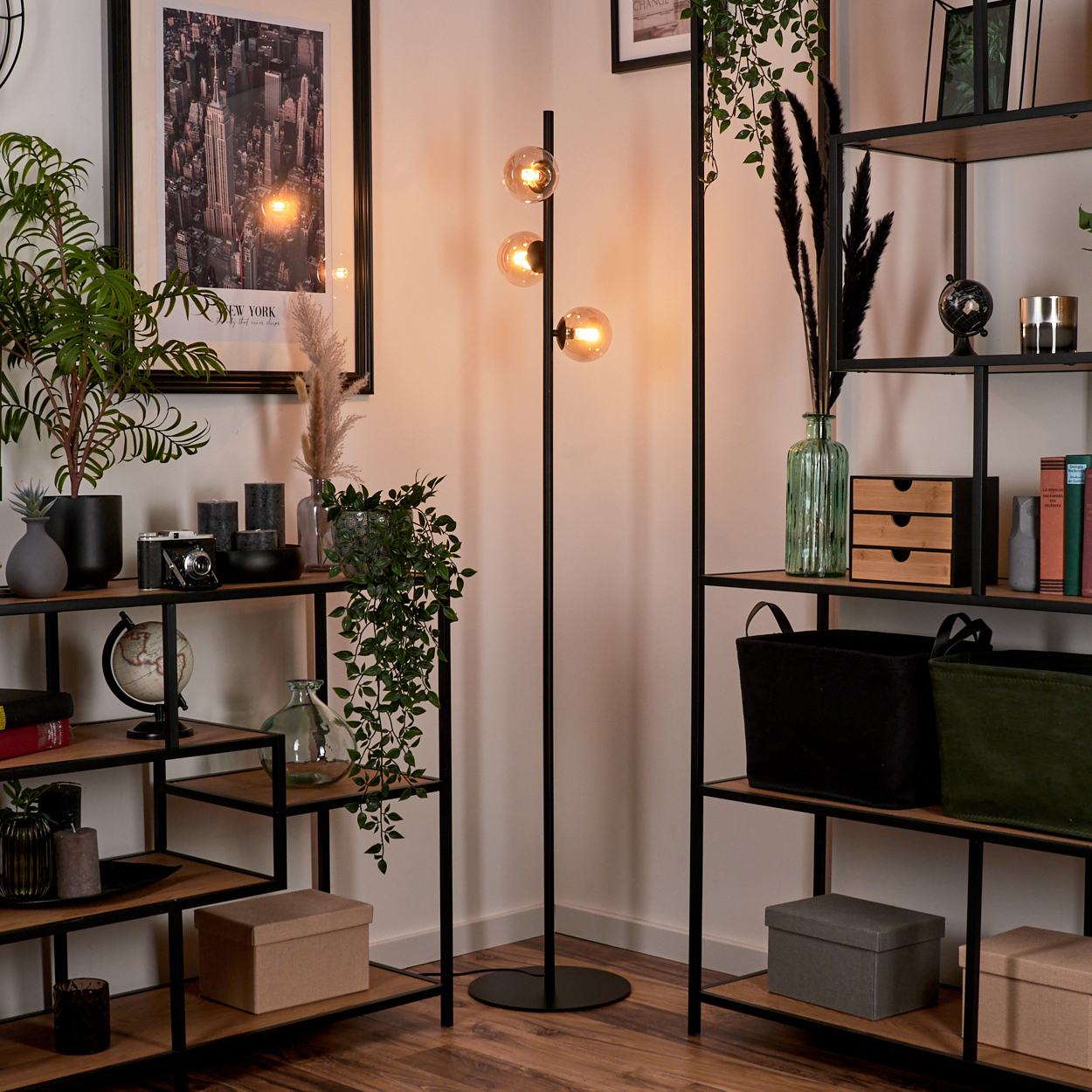 Schwarze Stehlampe mit drei Kugellampen neben Regalen mit Dekoration.