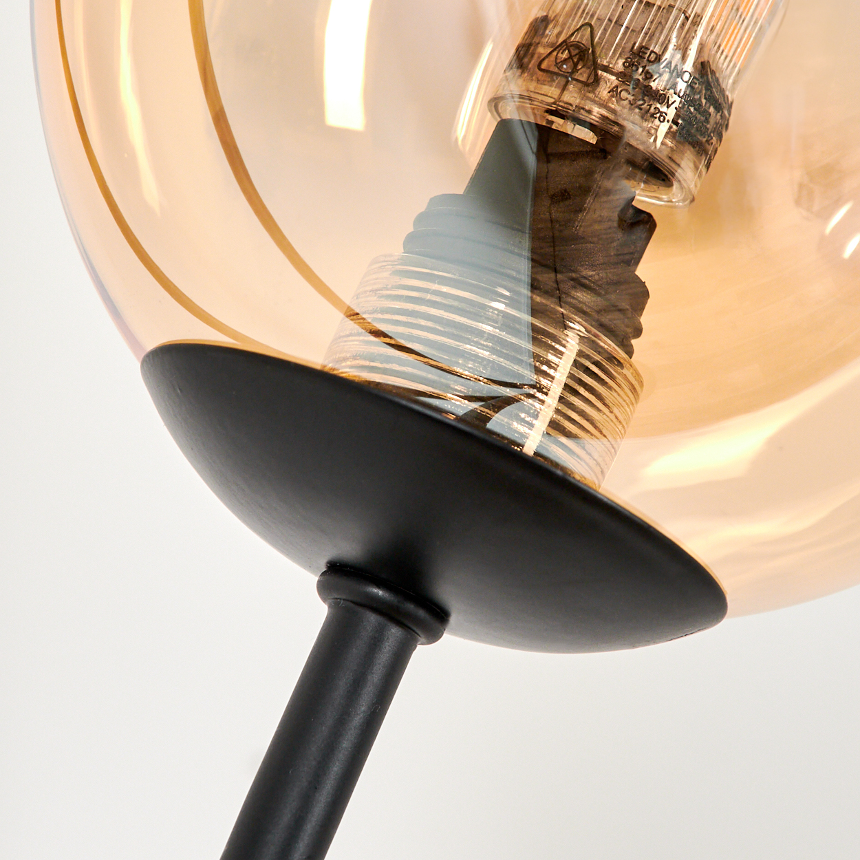 Nahaufnahme eines schwarzen Stiels, der eine bernsteinfarbene Glühbirne mit LED-Licht hält.