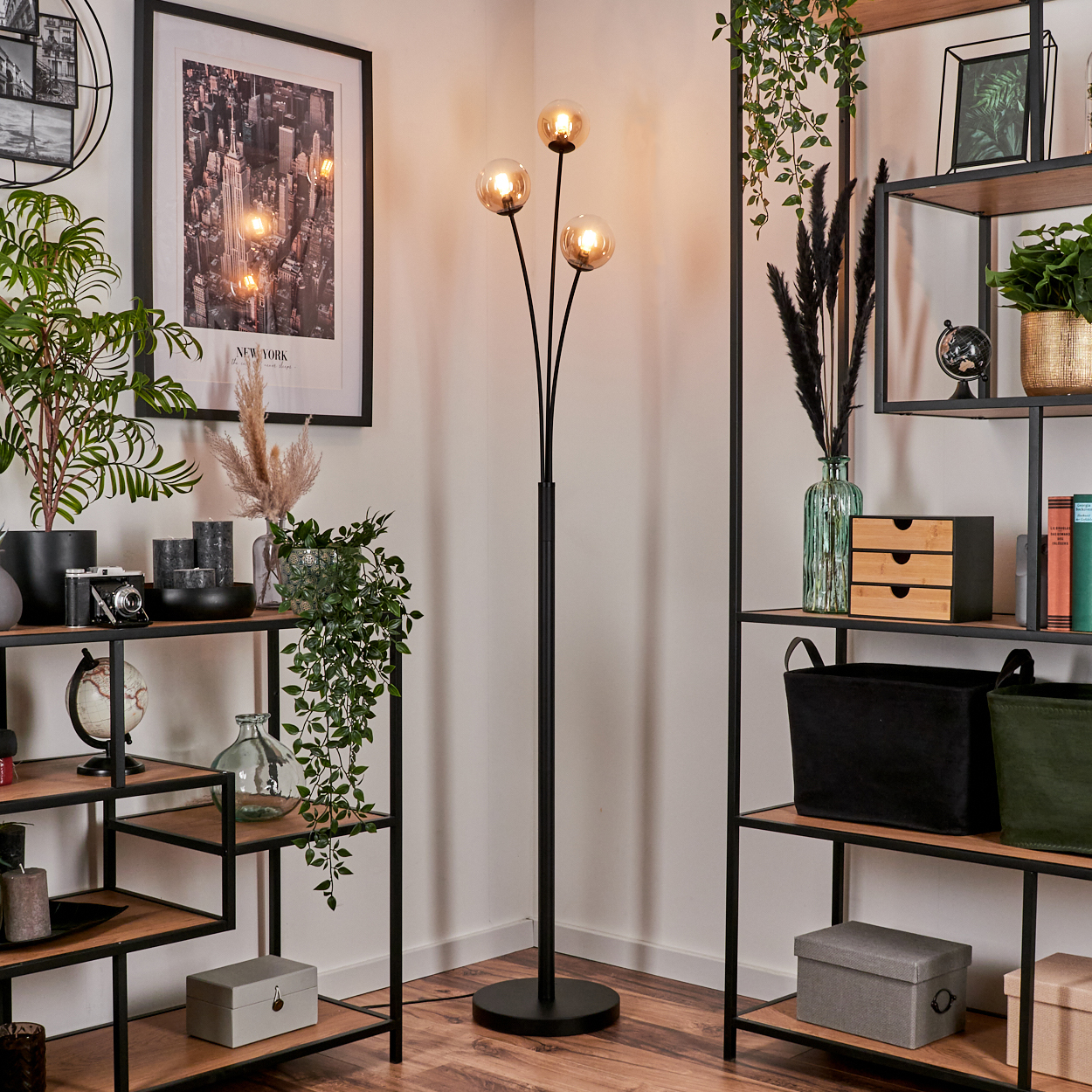 Schwarze Stehlampe mit drei Kugelleuchten, in einem Raum mit Dekoration und Regalen.