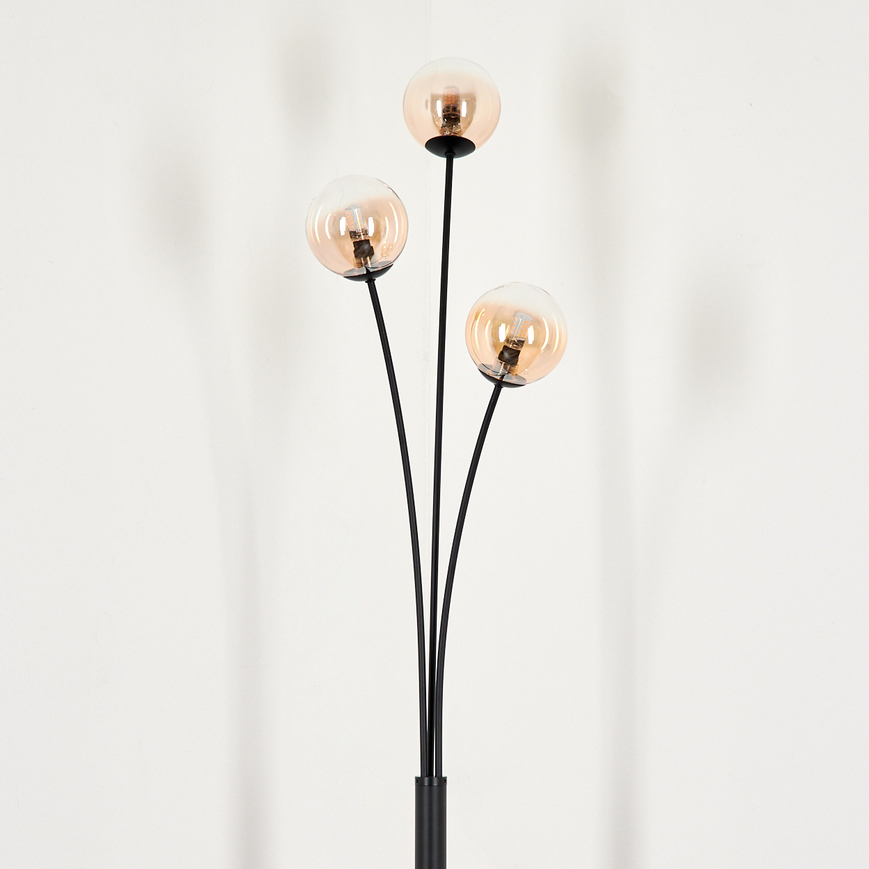 Schwarze Stehlampe mit drei bernsteinfarbenen Glasschirmen. Die Lampe steht vor weißem Hintergrund.