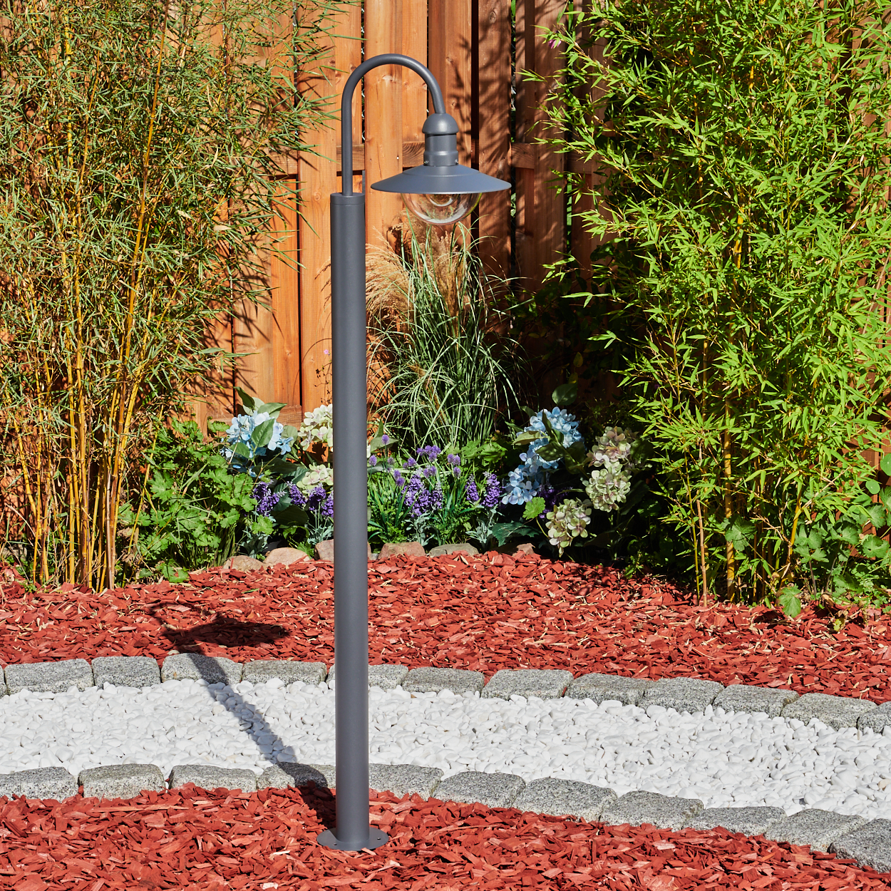 Graue Laterne in einem Garten mit roter Mulch und Steinweg.