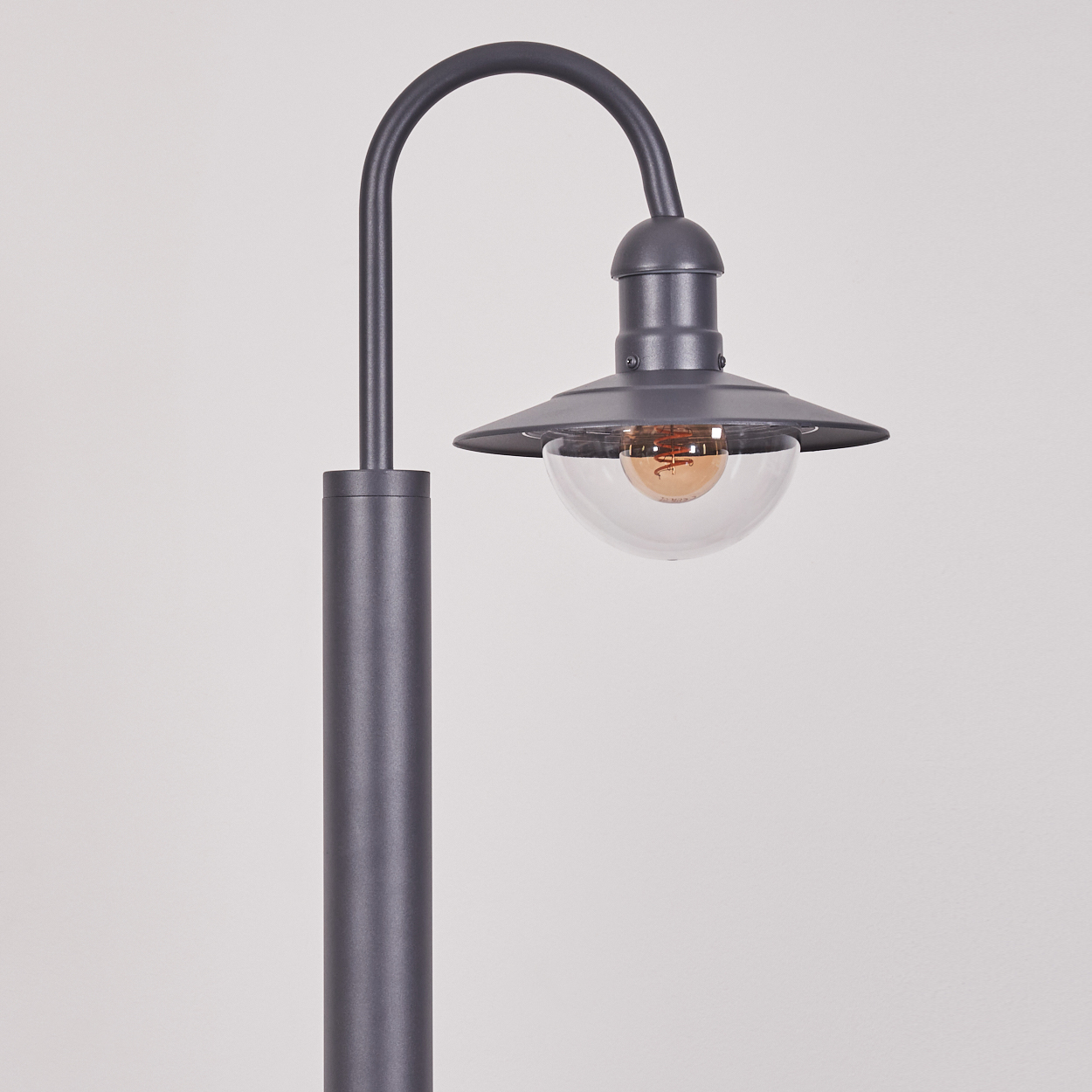 Grauer Außenlampenpfosten mit gebogenem Arm, der eine klare Glaskugel-Lampe hält. Weißer Hintergrund.